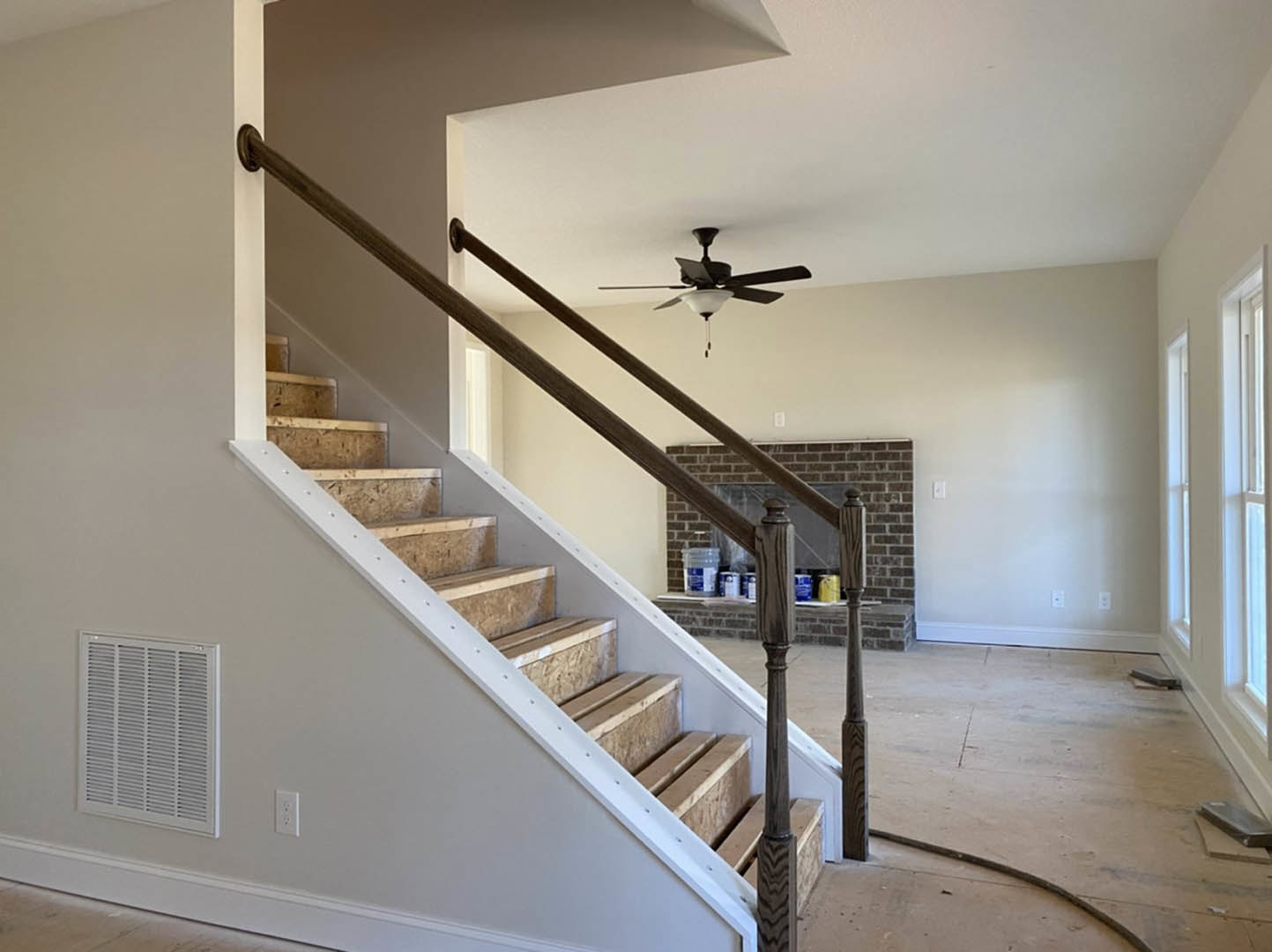 Wood plank staircase with dark metal handrail, white plaster walls, ceiling fan with light fixture, and decorative molding.