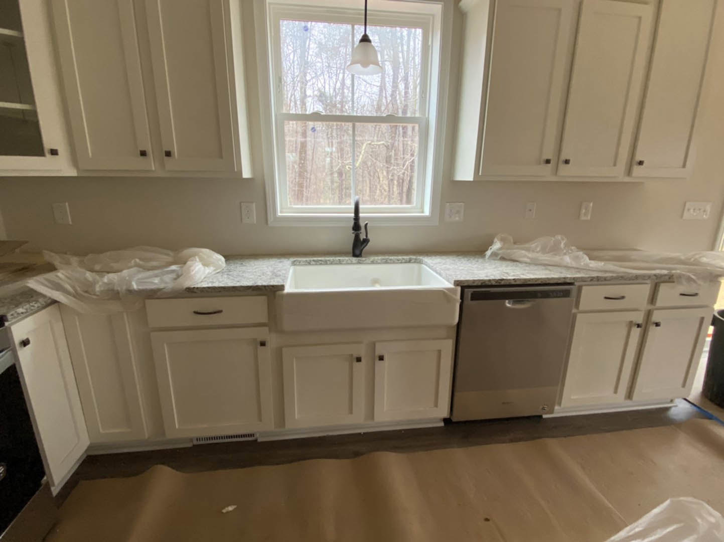 White kitchen cabinets with silver hardware, stainless steel dishwasher, undermount sink with chrome faucet, white countertop, window above sink letting in natural light.