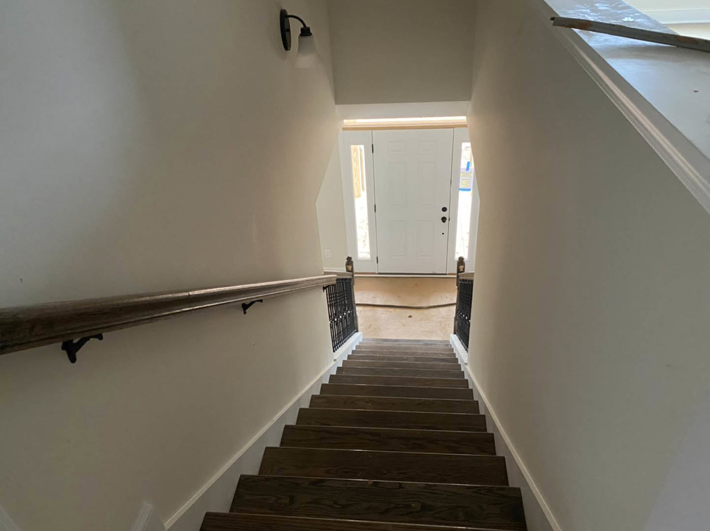 Wood staircase with metal handrail, white plaster walls, glass-paneled door, and wall-mounted light fixture