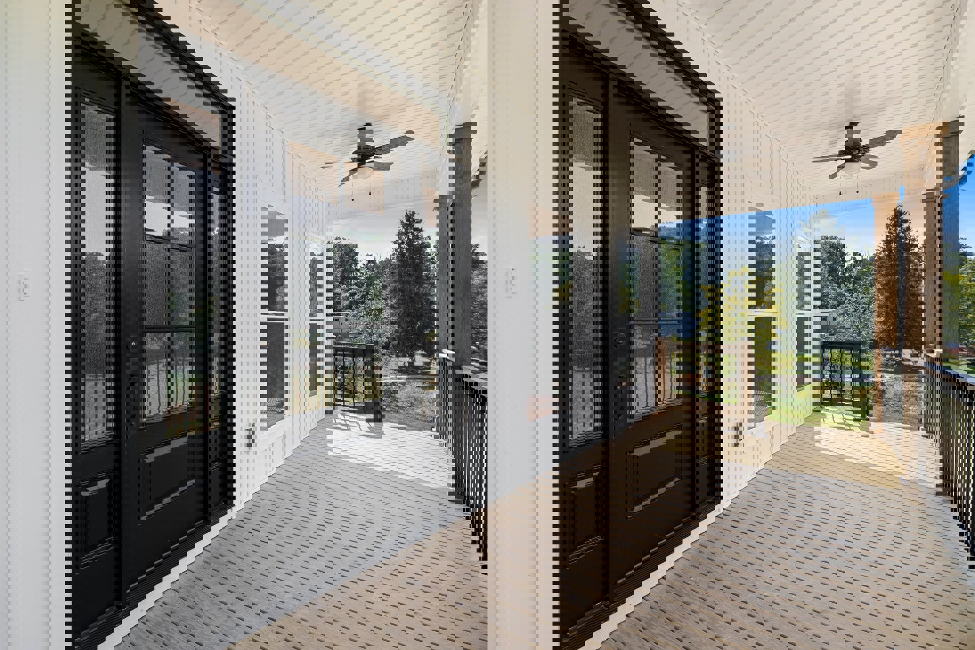 Wooden porch with a black door featuring glass panes, ceiling fan with light, leafy tree, and bulldozer visible through fence