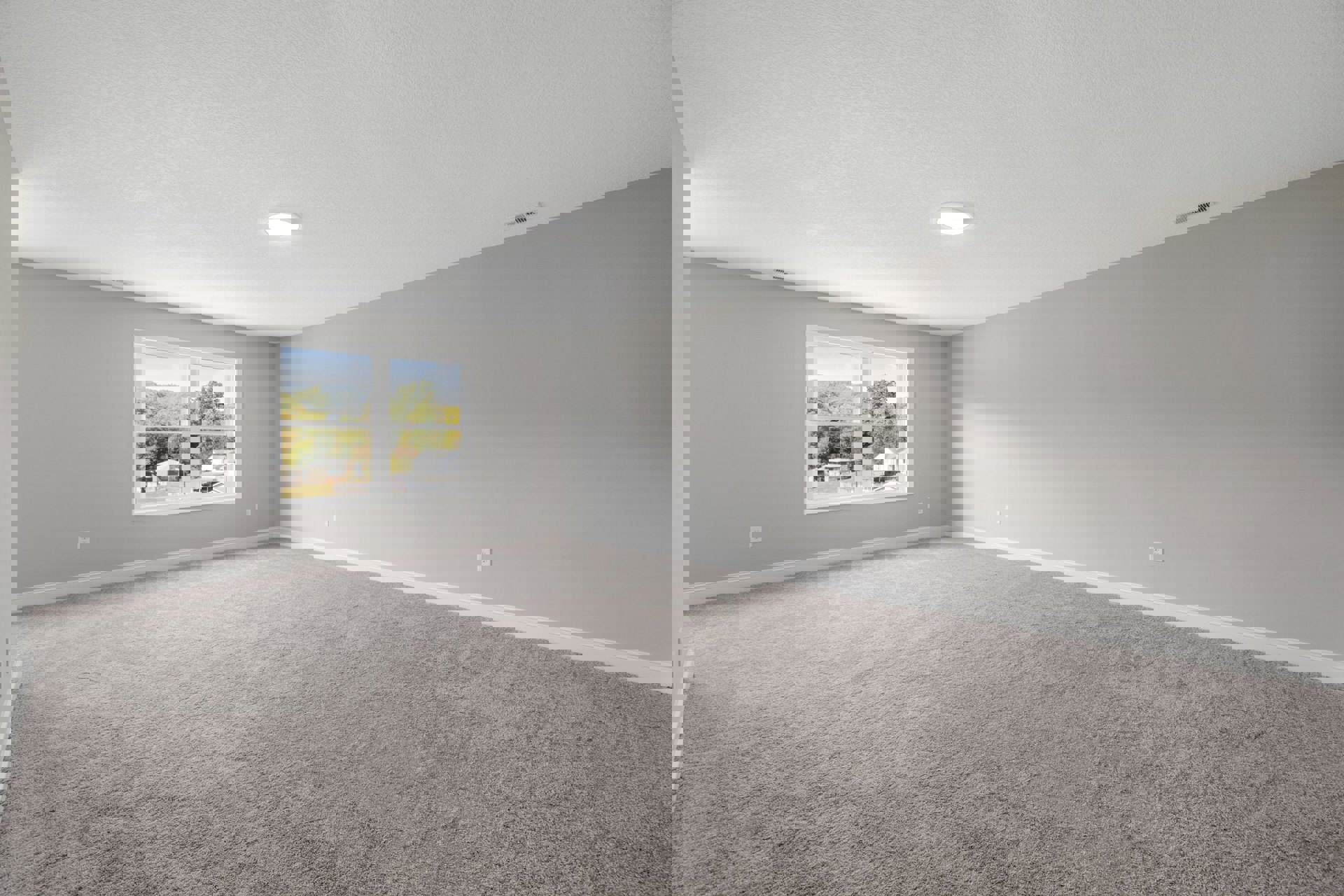 Carpeted room with white walls, large window overlooking neighborhood houses and distant trees, white ceiling with recessed light fixture