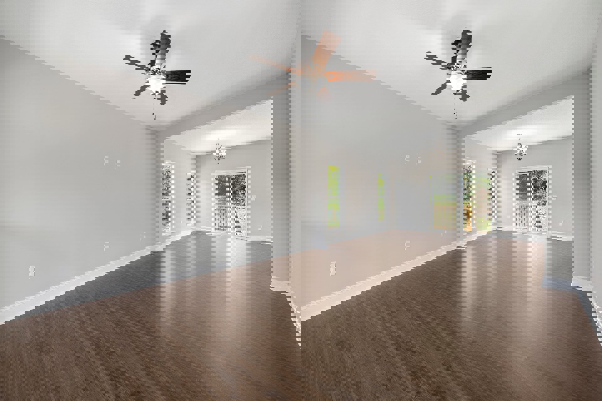 Ceiling fan with light fixture mounted on white plaster ceiling, hardwood flooring, sliding glass door, white-framed windows, and chandelier with white shade in spacious room