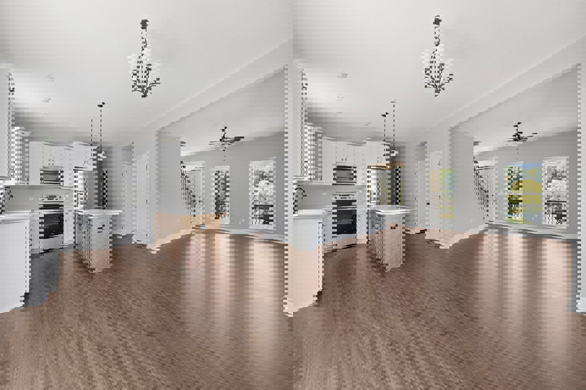 Spacious open floor plan featuring a kitchen island with white countertop, hardwood flooring, modern stove and oven, cabinetry, large window overlooking trees, and a chandelier