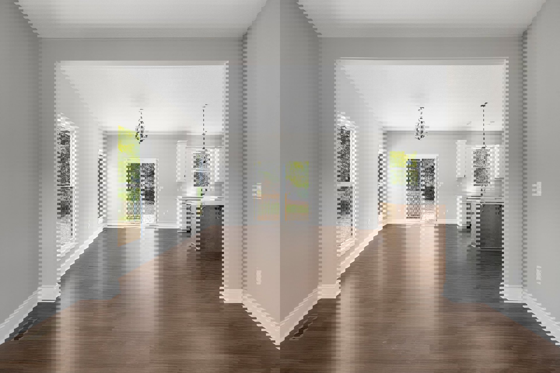 Spacious room with wood flooring, white walls, chandelier with white shades, sliding glass door overlooking yard, adjacent kitchen area, and floor vent