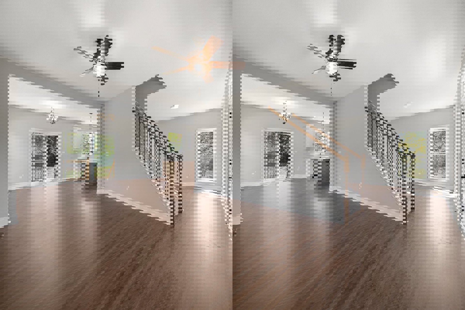 Spacious room with hardwood flooring, ceiling fan with light, metal-railed staircase, large window overlooking trees, and sliding glass door with exterior railing