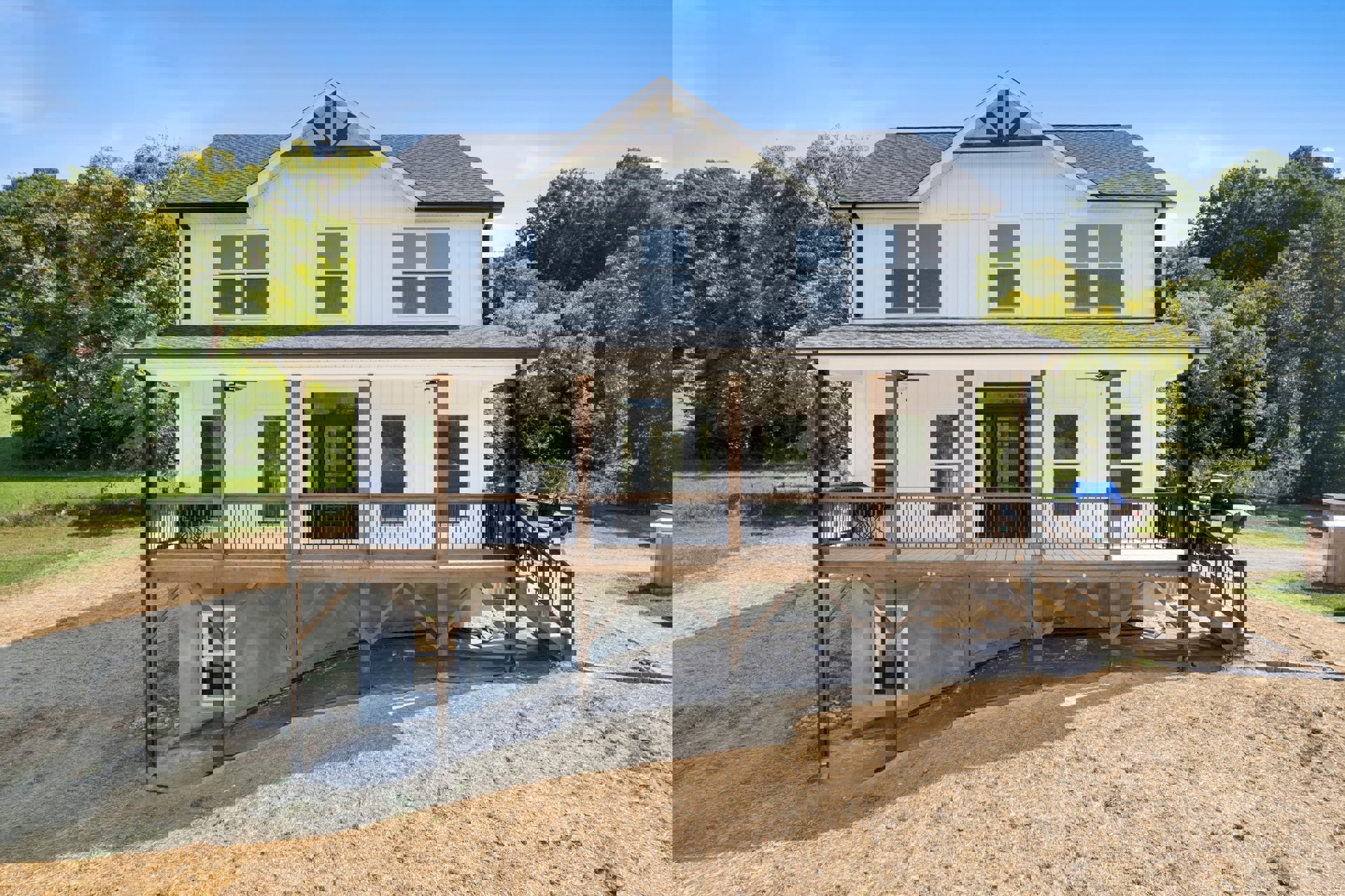 Wooden deck with accessibility ramp leading to front door, white-framed window, covered vehicle with blue tarp beside porch, trees and sky in background