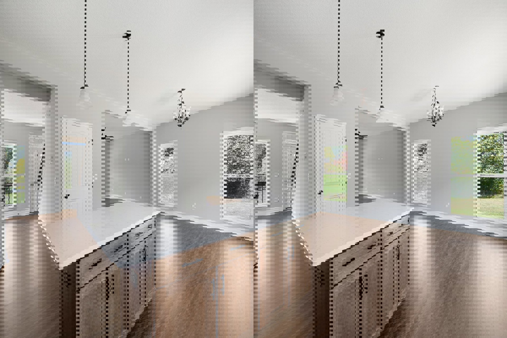 Kitchen with white marble island countertop, hardwood floors, white cabinetry, stainless steel sink, and windows overlooking green lawn and trees.