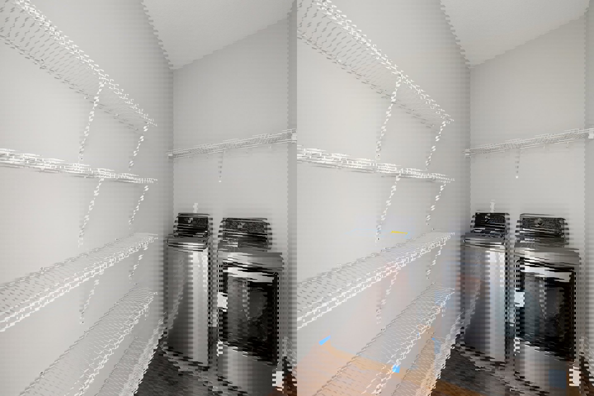 Laundry room with two front-loading dryers, white cabinetry, open shelving, and light-colored tile flooring