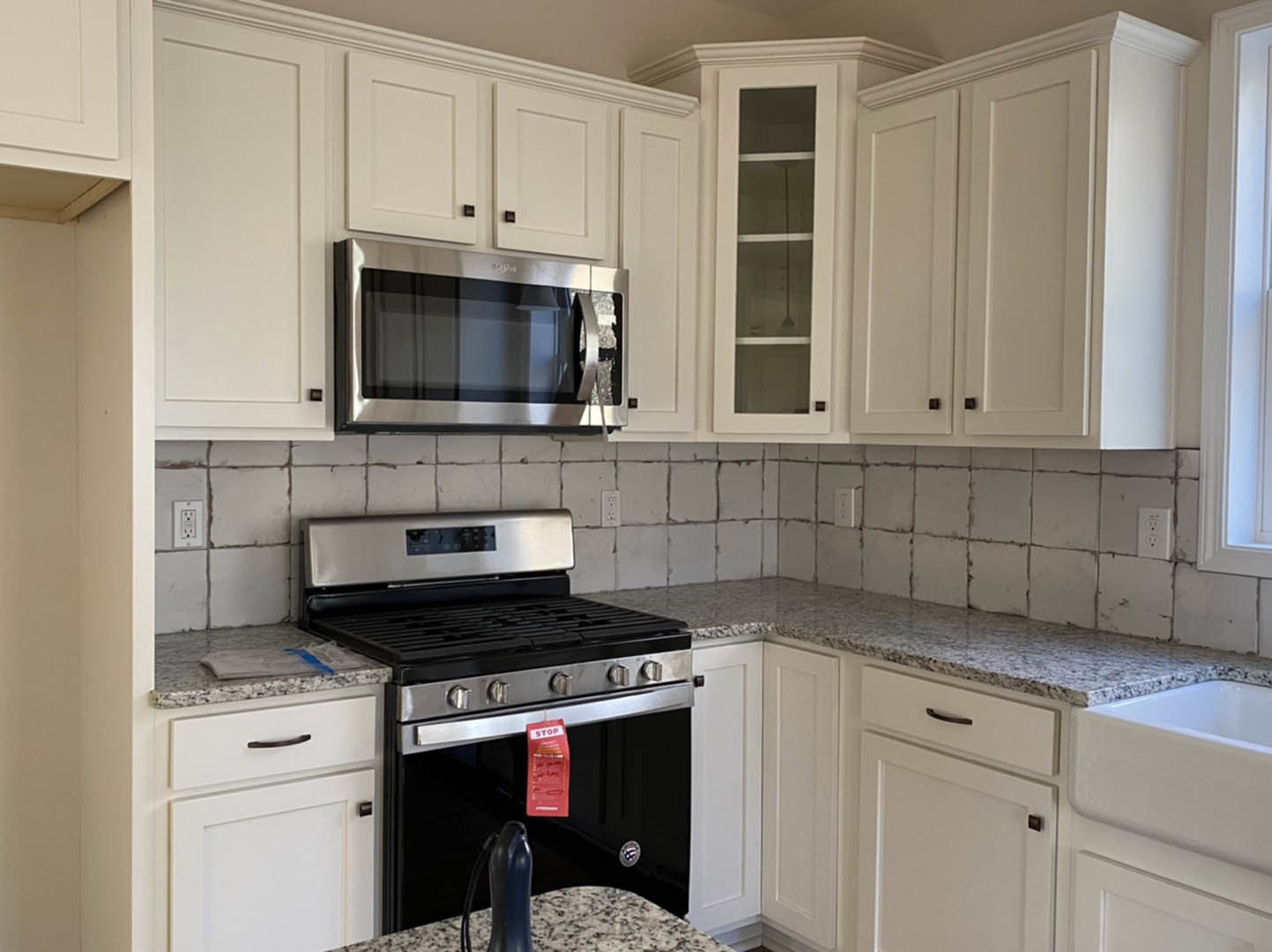 White shaker cabinets, black freestanding stove, stainless microwave above, light stone countertops, neutral tile backsplash, under-cabinet lighting