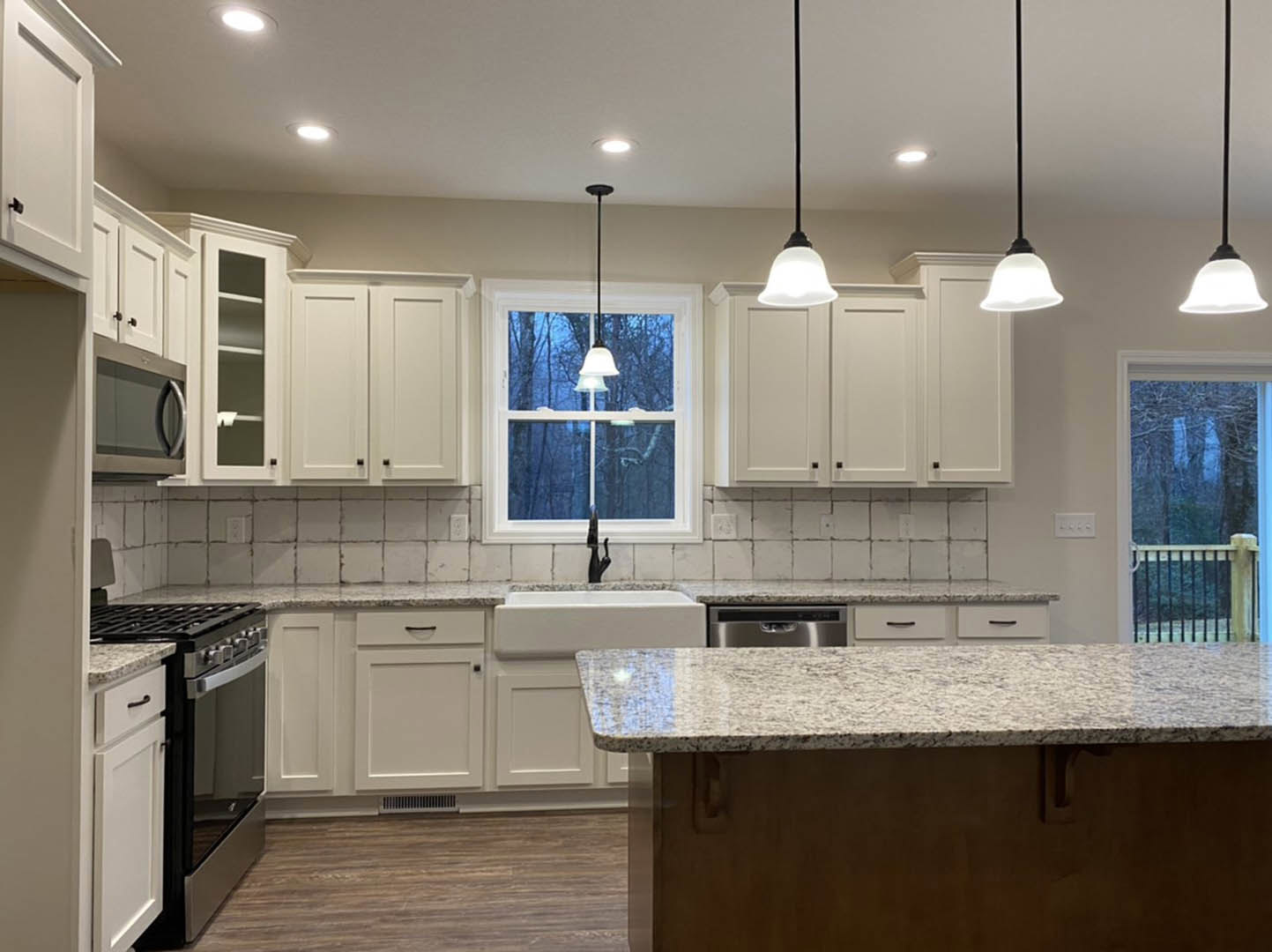 White kitchen cabinets, granite island with undermount sink, stainless steel appliances, pendant lighting, light walls, hardwood flooring