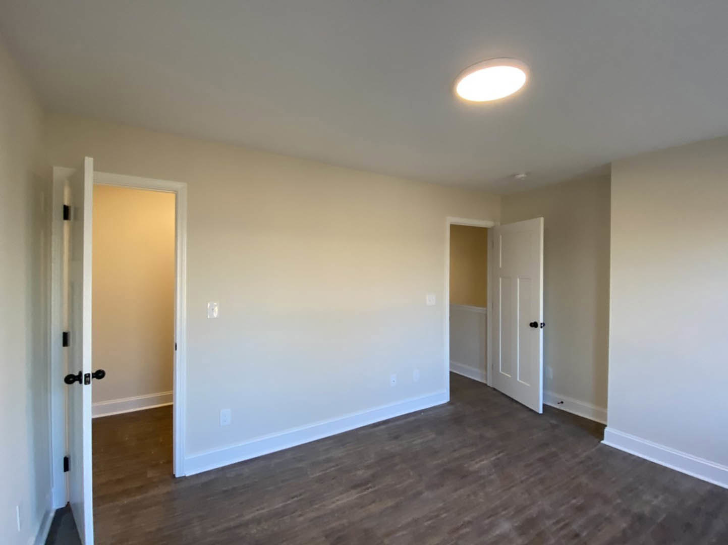 White walls with black trim, wood laminate flooring, white door, ceiling light fixture
