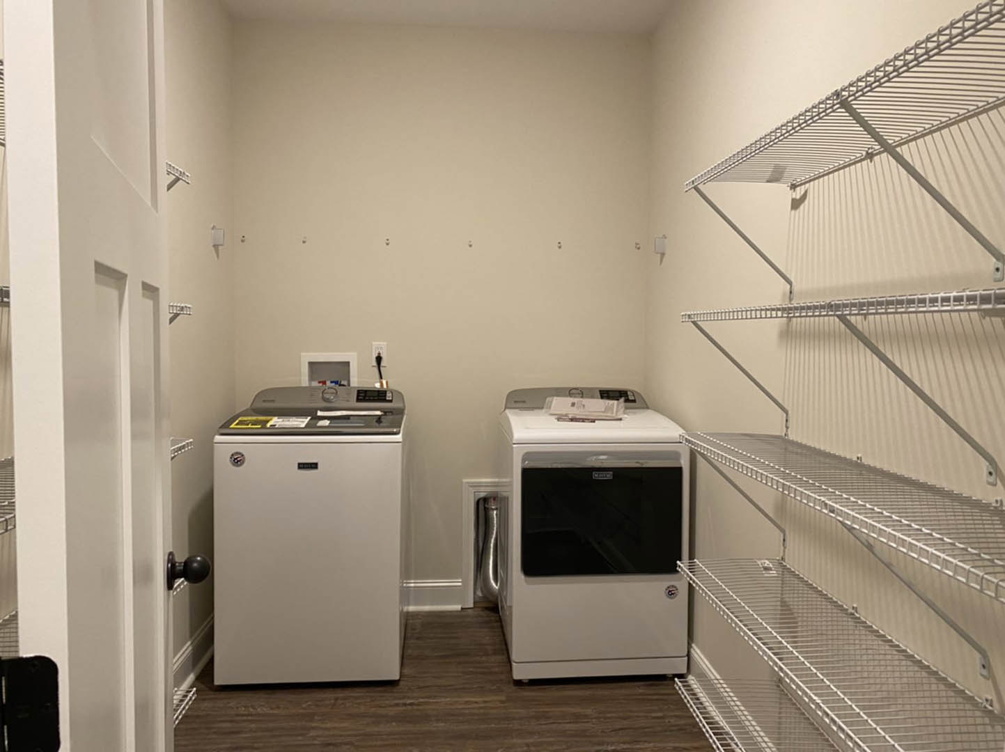 Laundry room with two white front-loading dryers, white cabinetry, light-colored flooring, and a small white refrigerator; close-up views of shelving and a silver door knob.