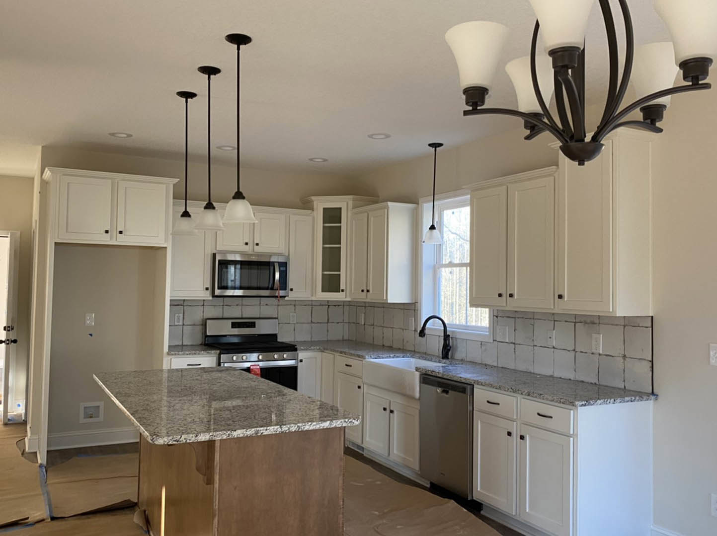 White kitchen cabinets, marble island countertop, stainless steel appliances, pendant lighting, undermount sink, light hardwood flooring