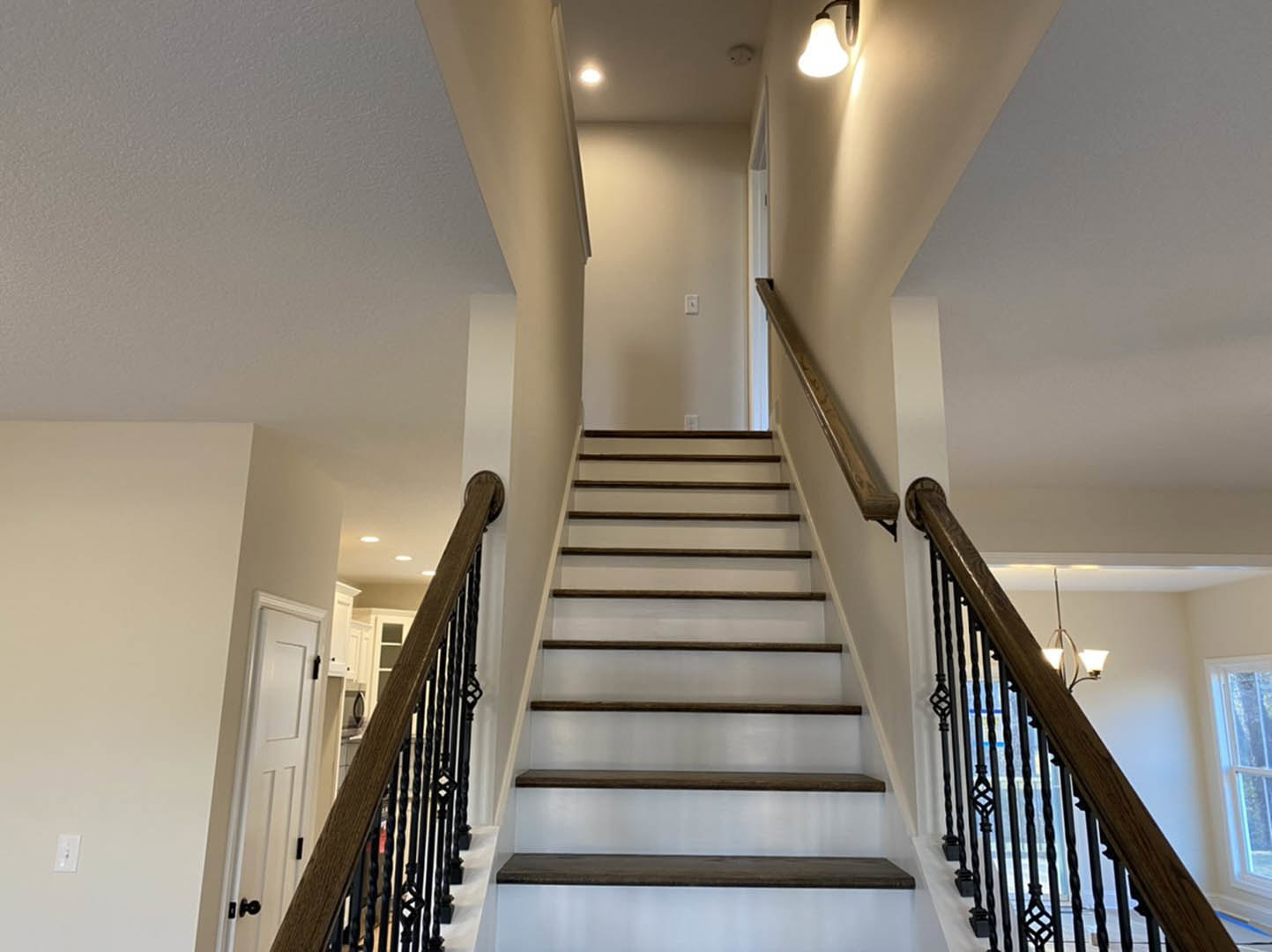 Wood staircase with black metal railing, white plaster walls, light fixture overhead, and hardwood flooring