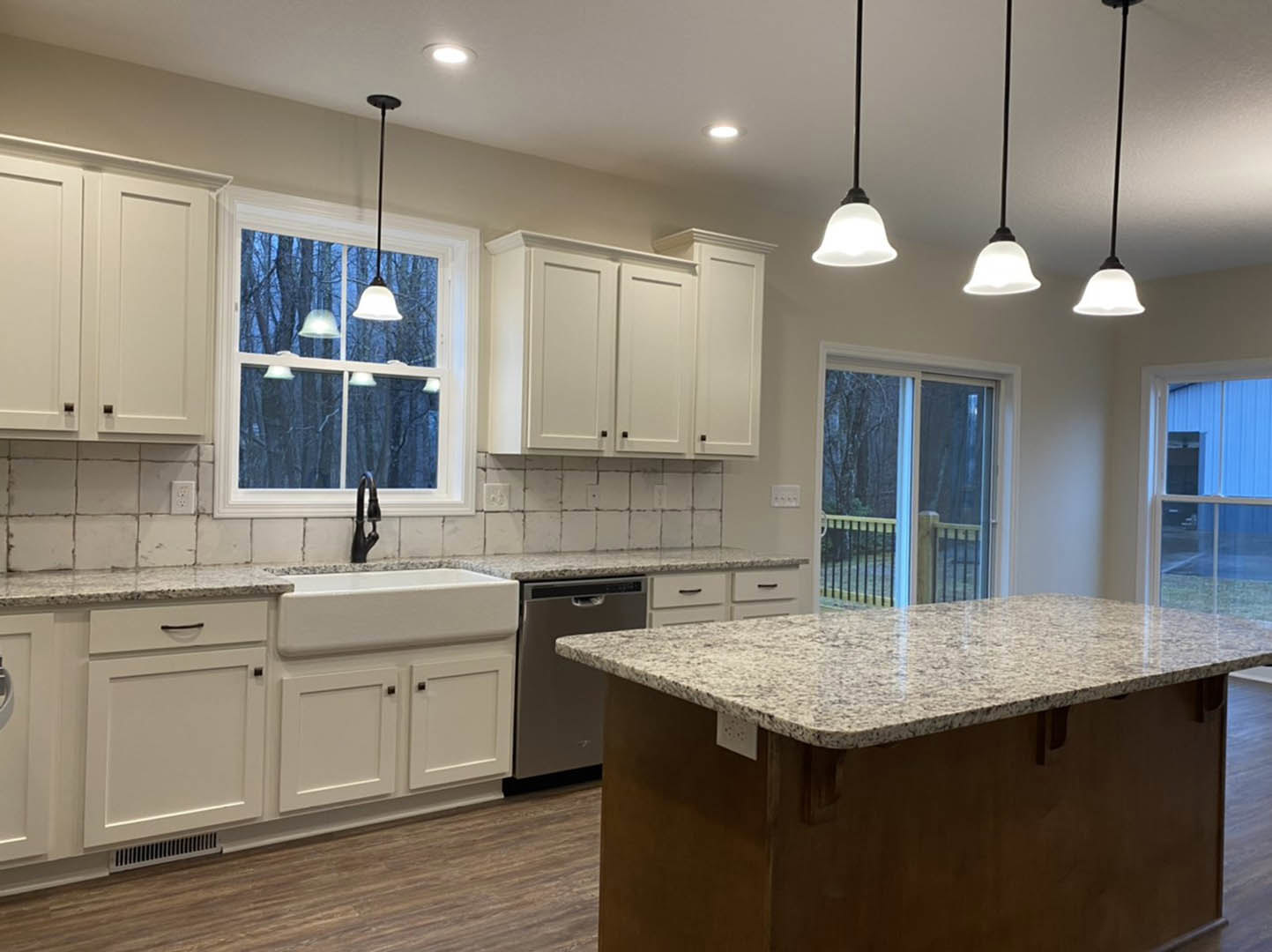 Spacious kitchen featuring a marble-topped island with built-in sink, white cabinetry, tile backsplash, sliding glass door with metal railing, and blue accent wall beneath windows
