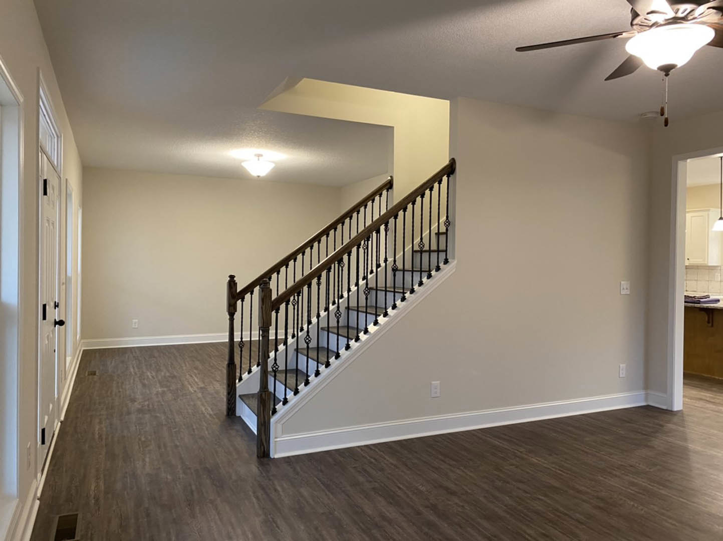 Wood staircase with black metal railings, light fixture and ceiling fan above, laminate flooring, white plaster walls, close-up of paneled door.