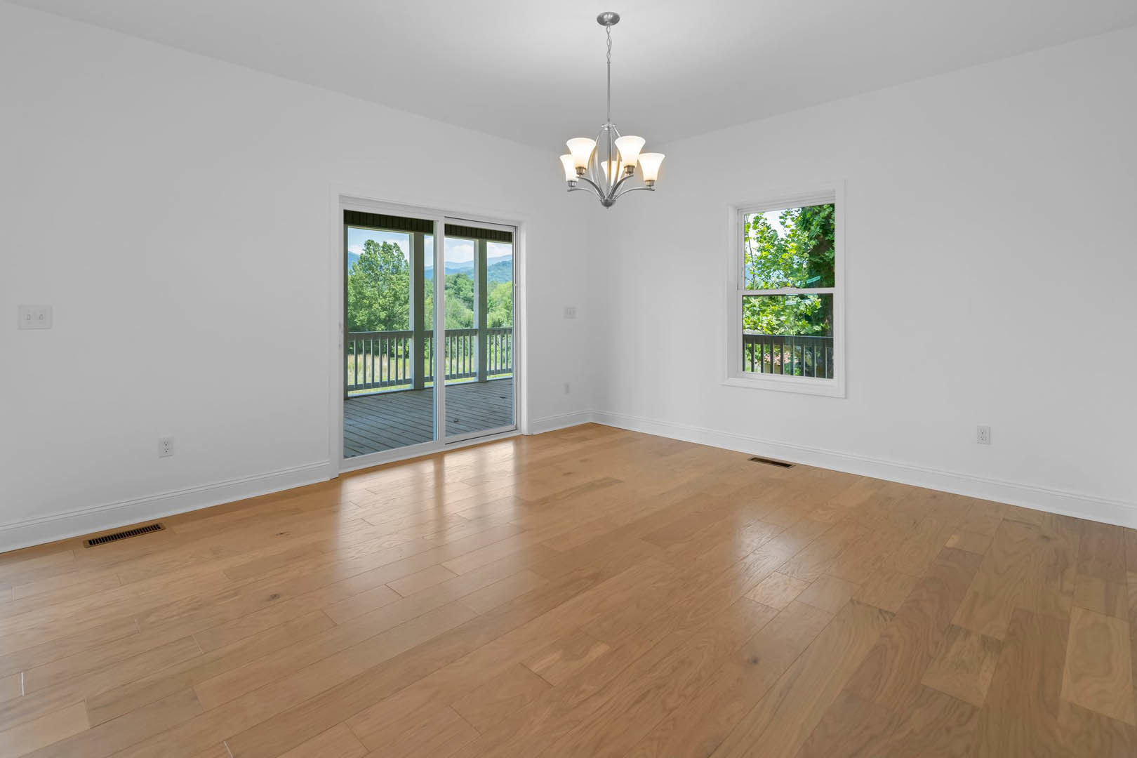 Hardwood floor room featuring a five-light chandelier, sliding glass door opening to mountain and tree views, and a window with greenery outside