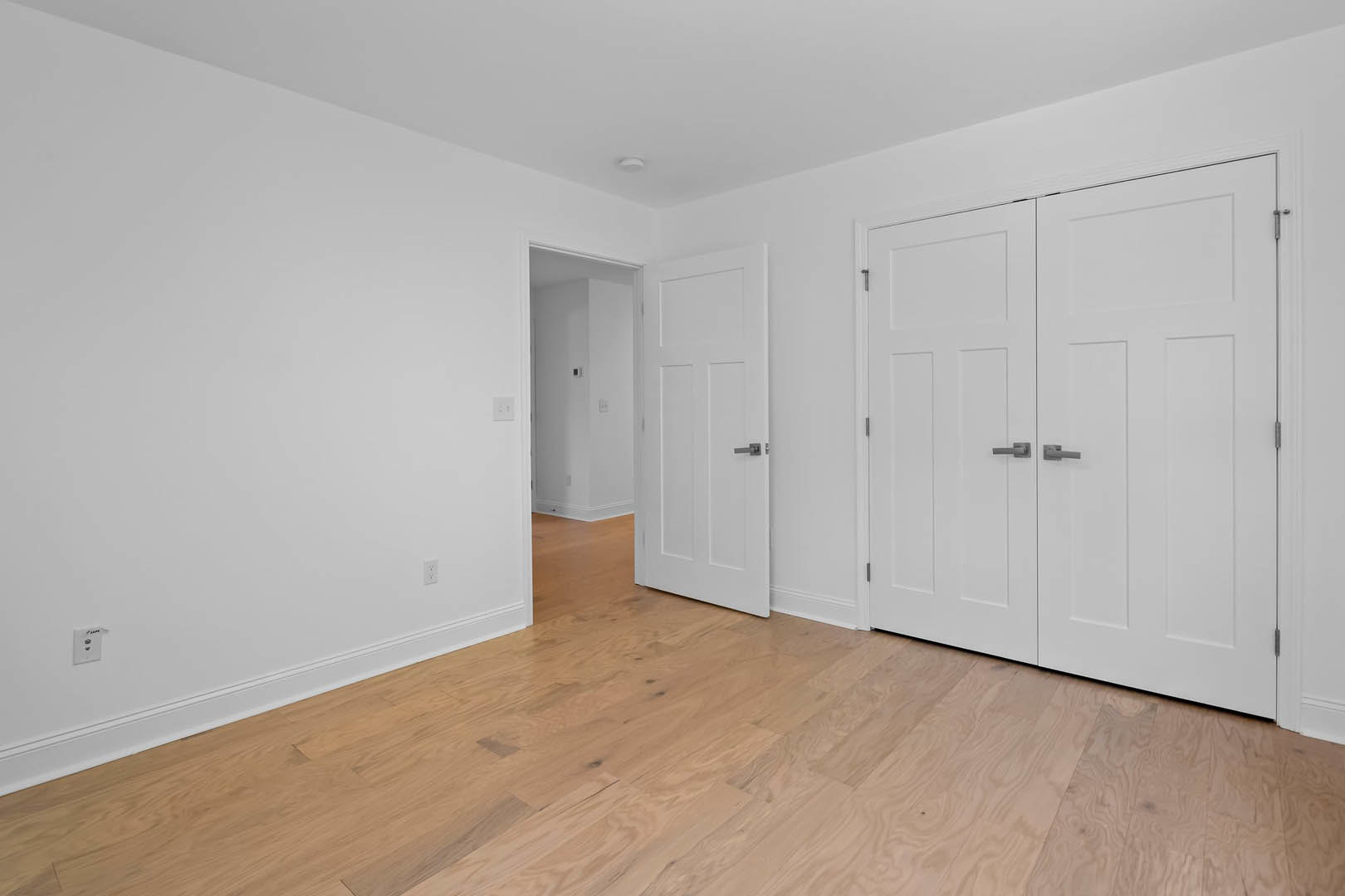 Hardwood floor room featuring white double doors with silver handles, white walls, and a wall-mounted rectangular control panel