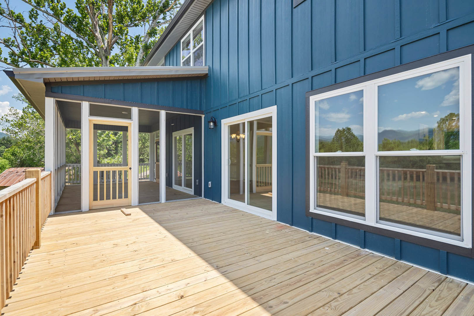 Blue siding home with wooden deck, glass door, screen door, light fixture, and view of trees; close-up of wood patio fence.