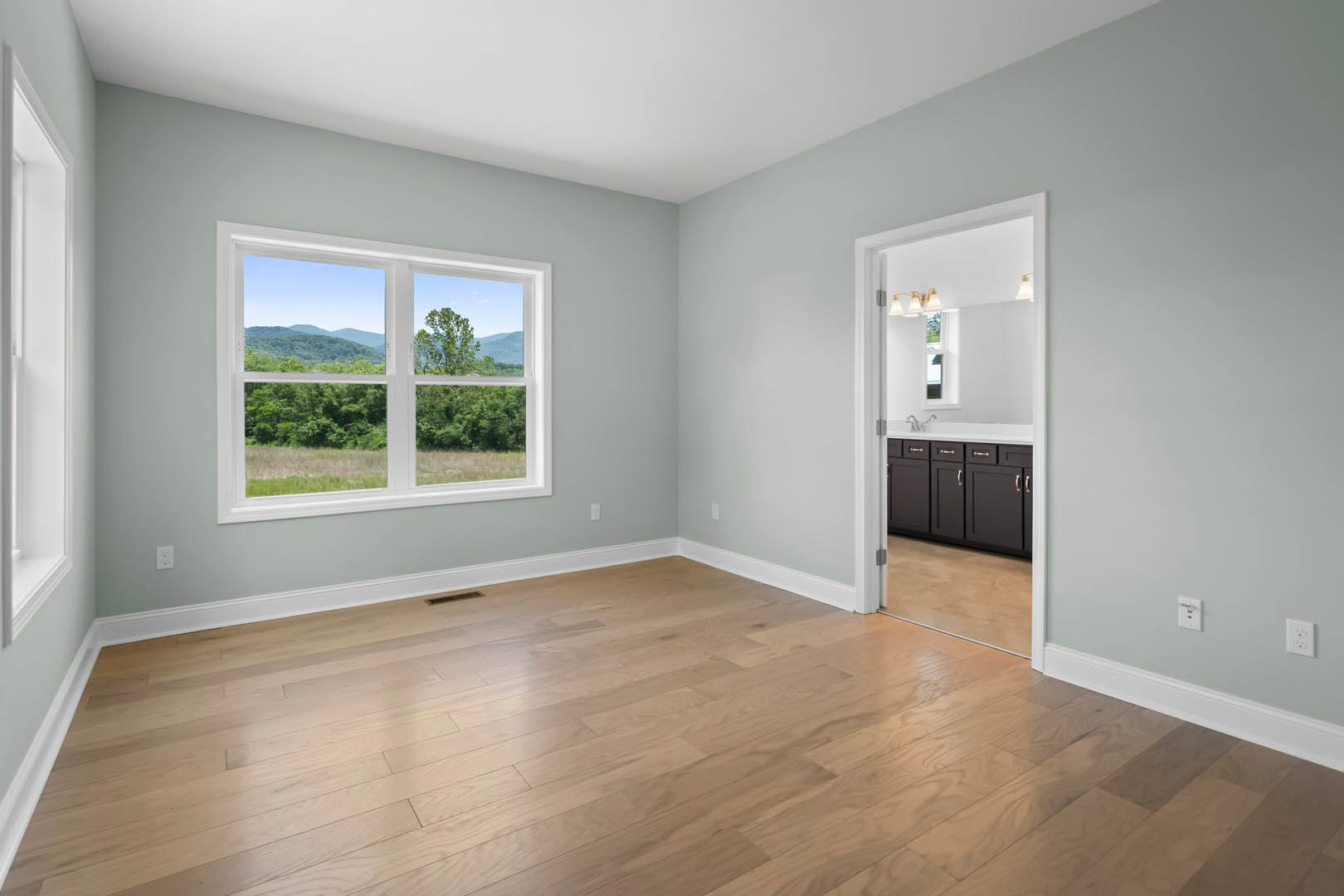 Wood-floored room with white baseboards, large window overlooking field and trees, neutral walls, natural light illuminating interior