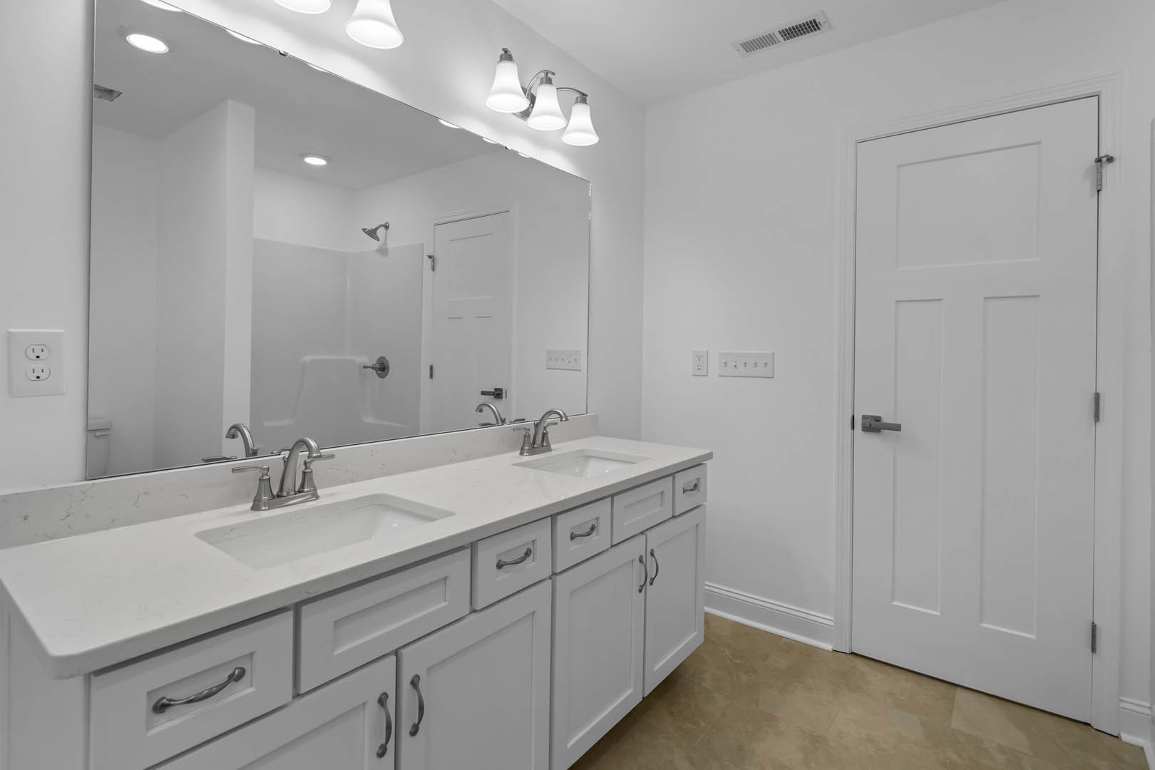 Bathroom with white cabinets and white countertops, white door with handle, close-up of sink and faucet, three-light fixture above mirror, vent in white wall, tile flooring