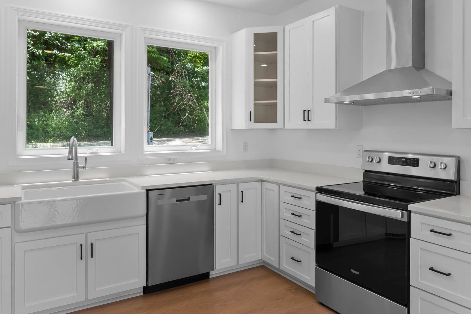 White kitchen cabinets, stainless steel stove and dishwasher, under-cabinet lighting, window with forest view, tree branches visible outside