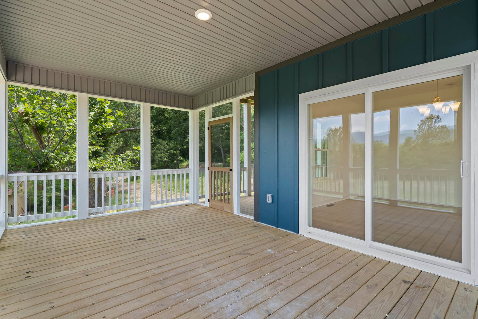 Spacious wooden porch featuring a blue door, sliding glass doors, ceiling light fixture, and deck flooring