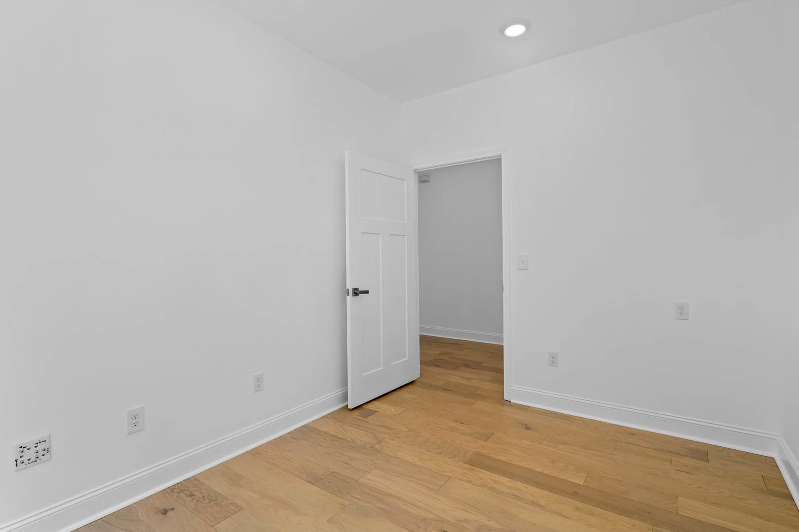 White paneled door with silver handle set in a white wall, black-framed trim, wood laminate flooring, and a white electrical outlet with black writing.