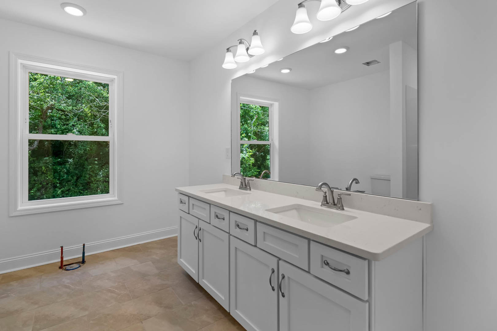 Bathroom with white shaker cabinets, expansive mirror above countertop, tile flooring, window overlooking trees, recessed ceiling lights, sink with chrome faucet, tools scattered