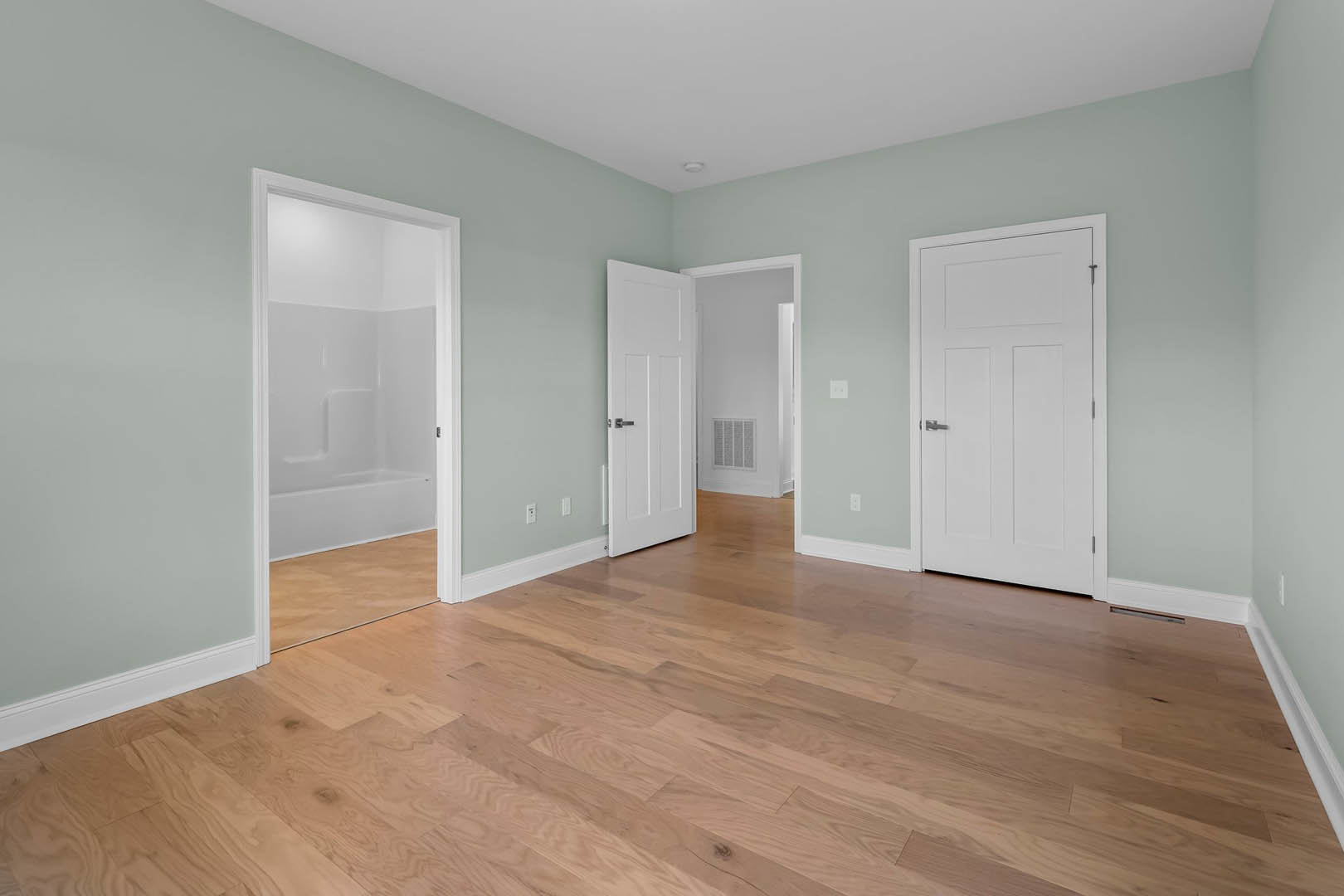 Bathroom with white paneled doors, freestanding bathtub, hardwood flooring, open glass shower stall, white walls with vent, and ceiling light fixture