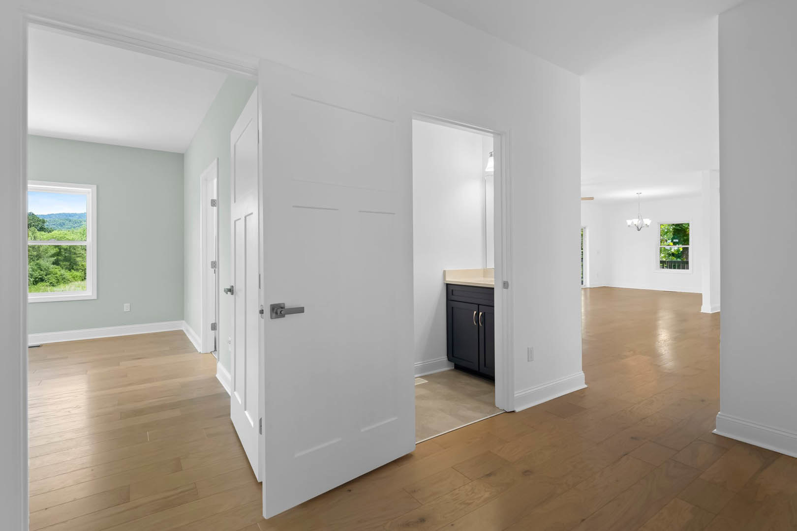 Hardwood floors, white doors with silver handles, black cabinet, large window framing trees and distant mountains