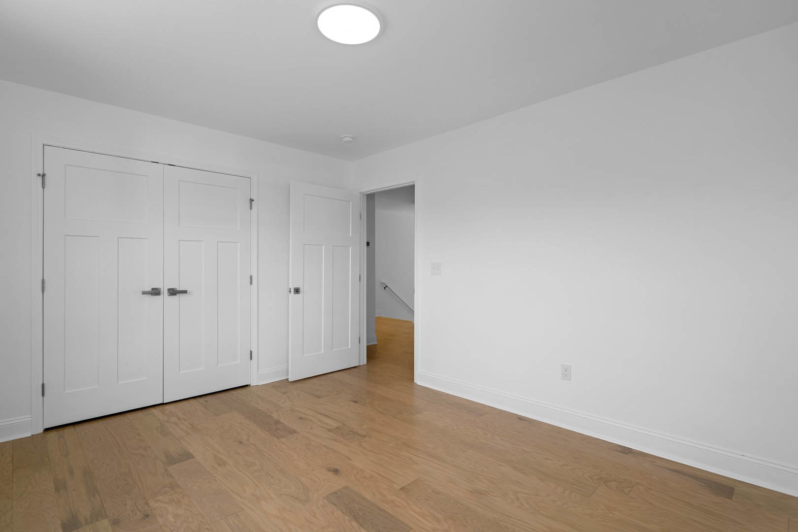 Hardwood floor with white double doors, silver handles, white walls, and a handrail
