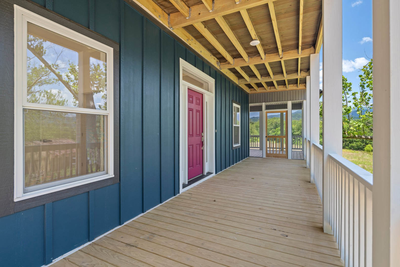 Wooden porch with a bold red door, white-framed windows, and natural decking
