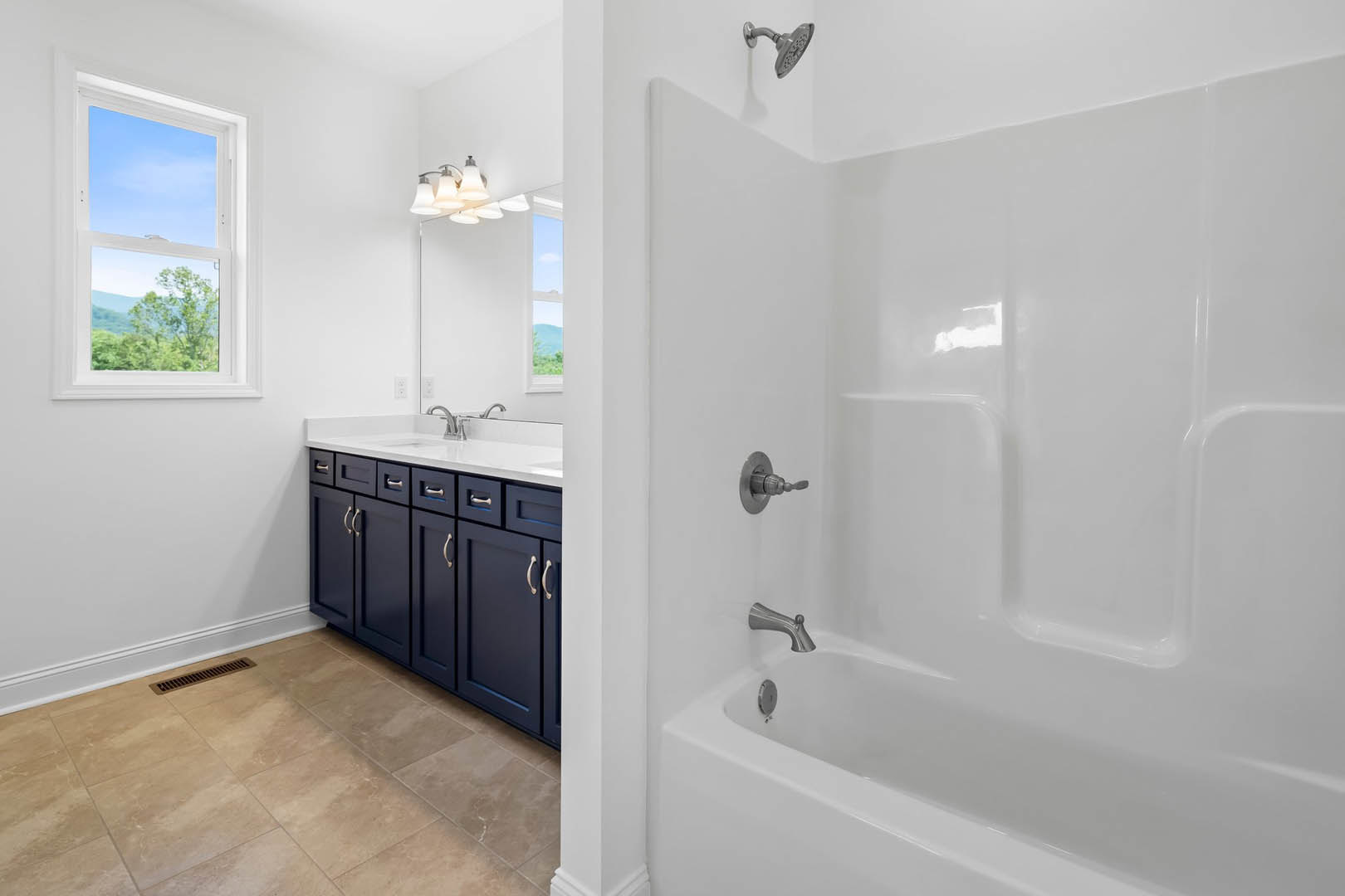 Bathroom featuring a white bathtub with silver faucets, blue cabinetry, tile flooring with a vent, a window overlooking a tree, and a shower head with nozzle.