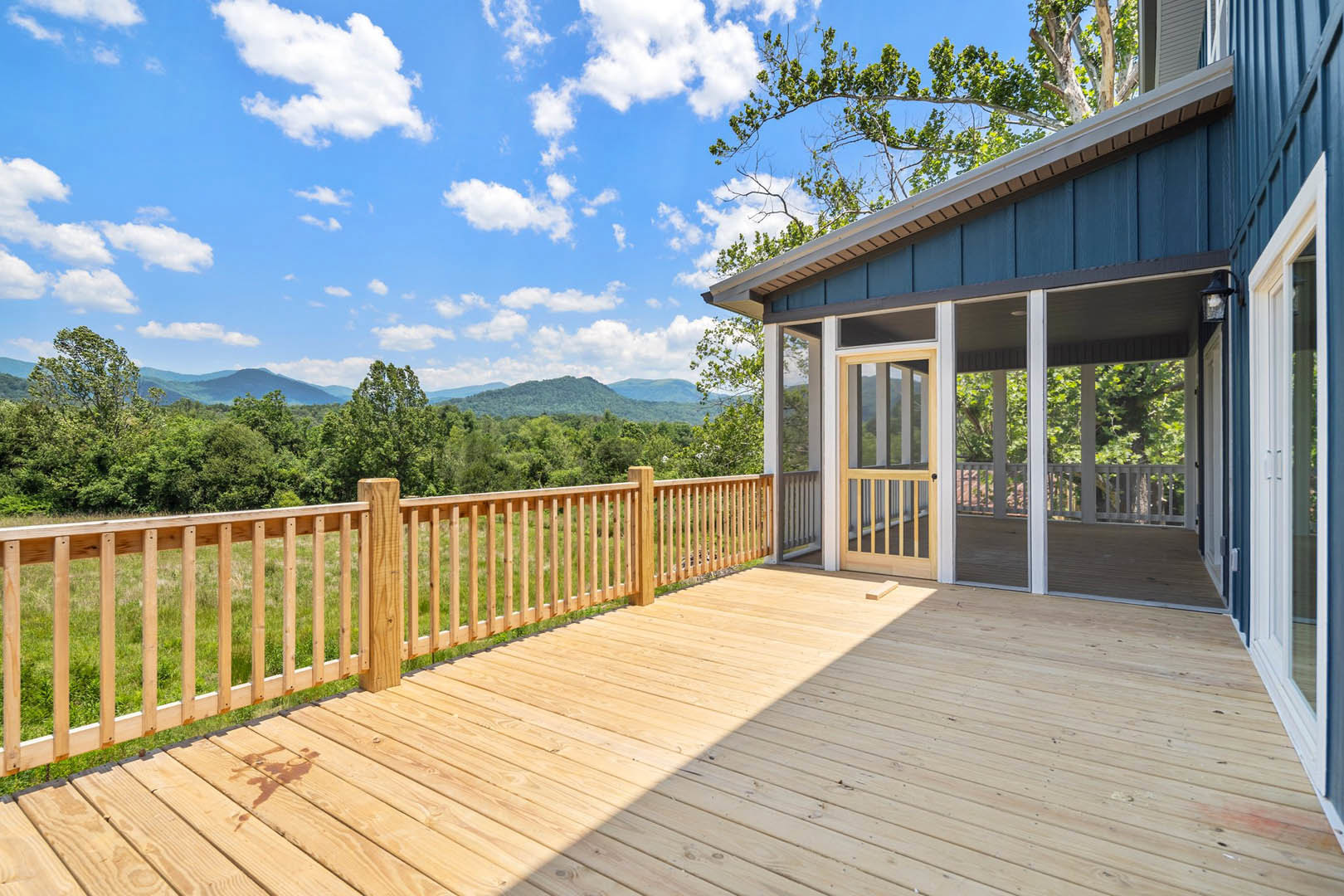 Wooden deck with screened porch, white railing fence, surrounded by trees under blue sky
