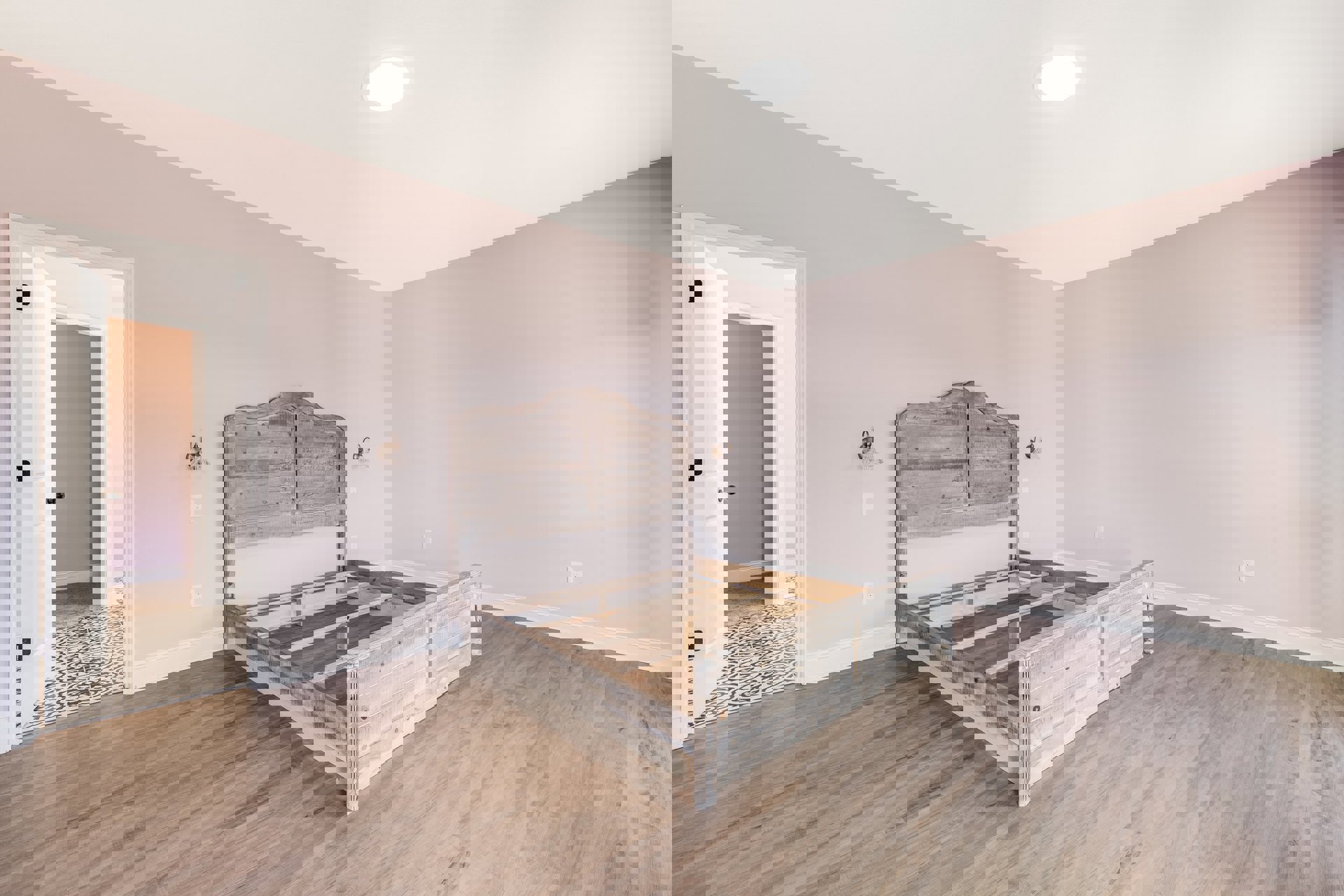 Wooden bed frame with matching headboard against a white plaster wall, laminate wood flooring, white door with black handle, ceiling light fixture