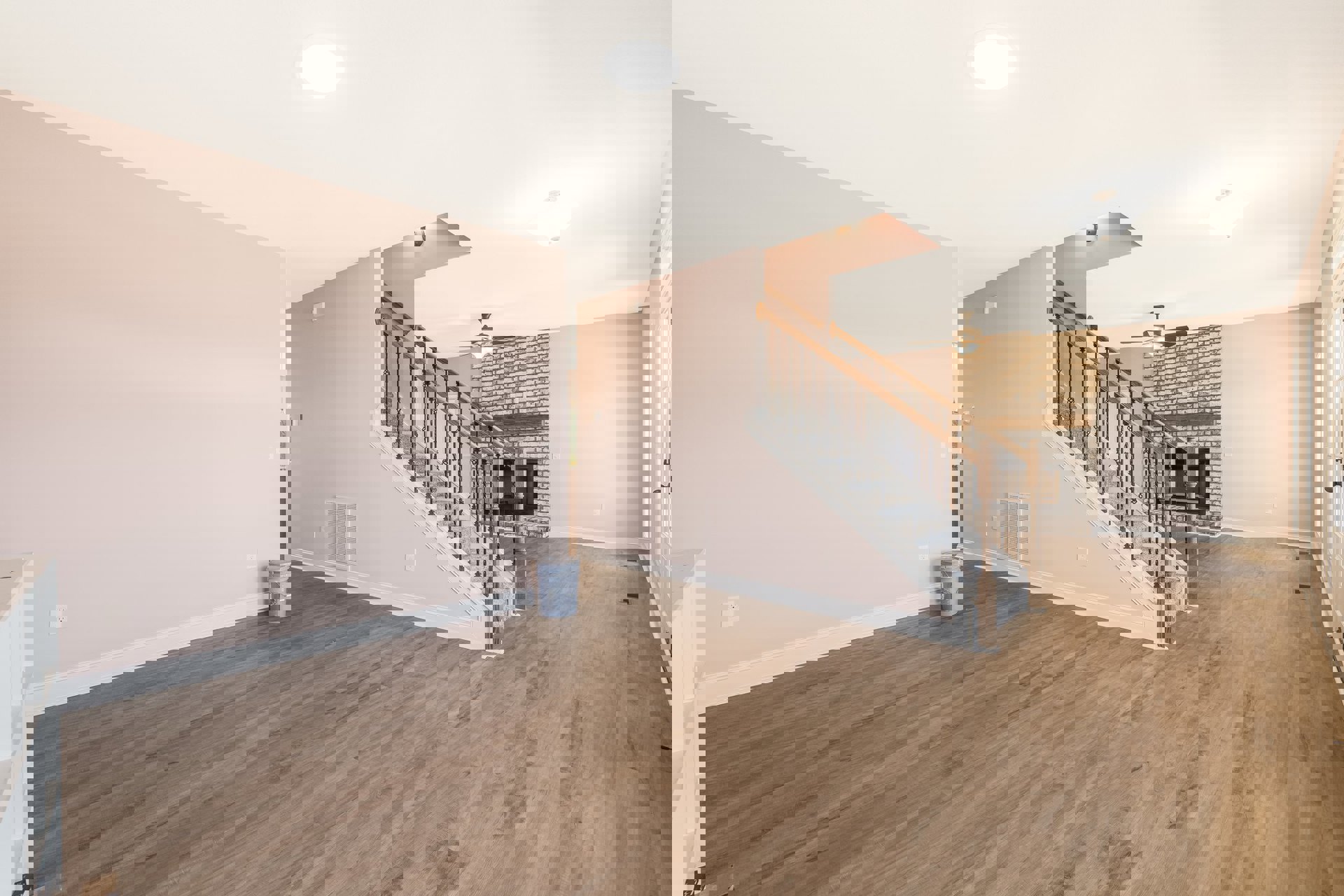 Open living area with wood flooring, white ceiling fan, brick accent wall, modern staircase with metal handrail, and stone fireplace