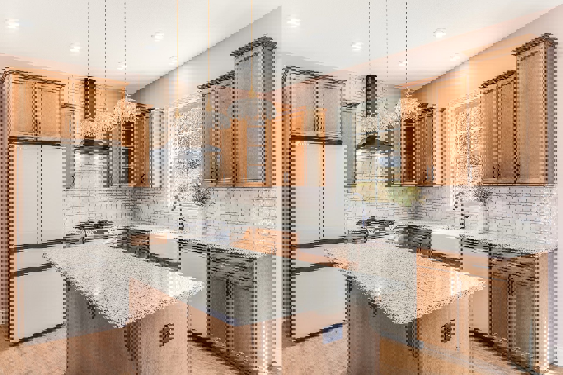 Marble countertop kitchen with white appliances, black and white cabinetry, black wall outlet, vase of flowers, window overlooking trees and grass