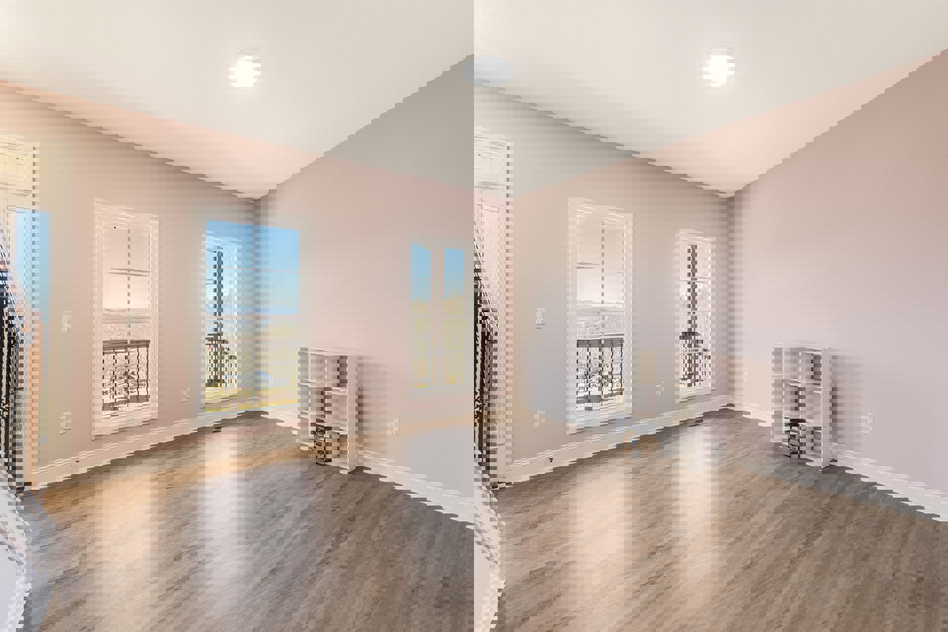 Wood floor room with large window overlooking landscape, white built-in shelf filled with books, round ceiling light fixture, white plaster walls and decorative molding.