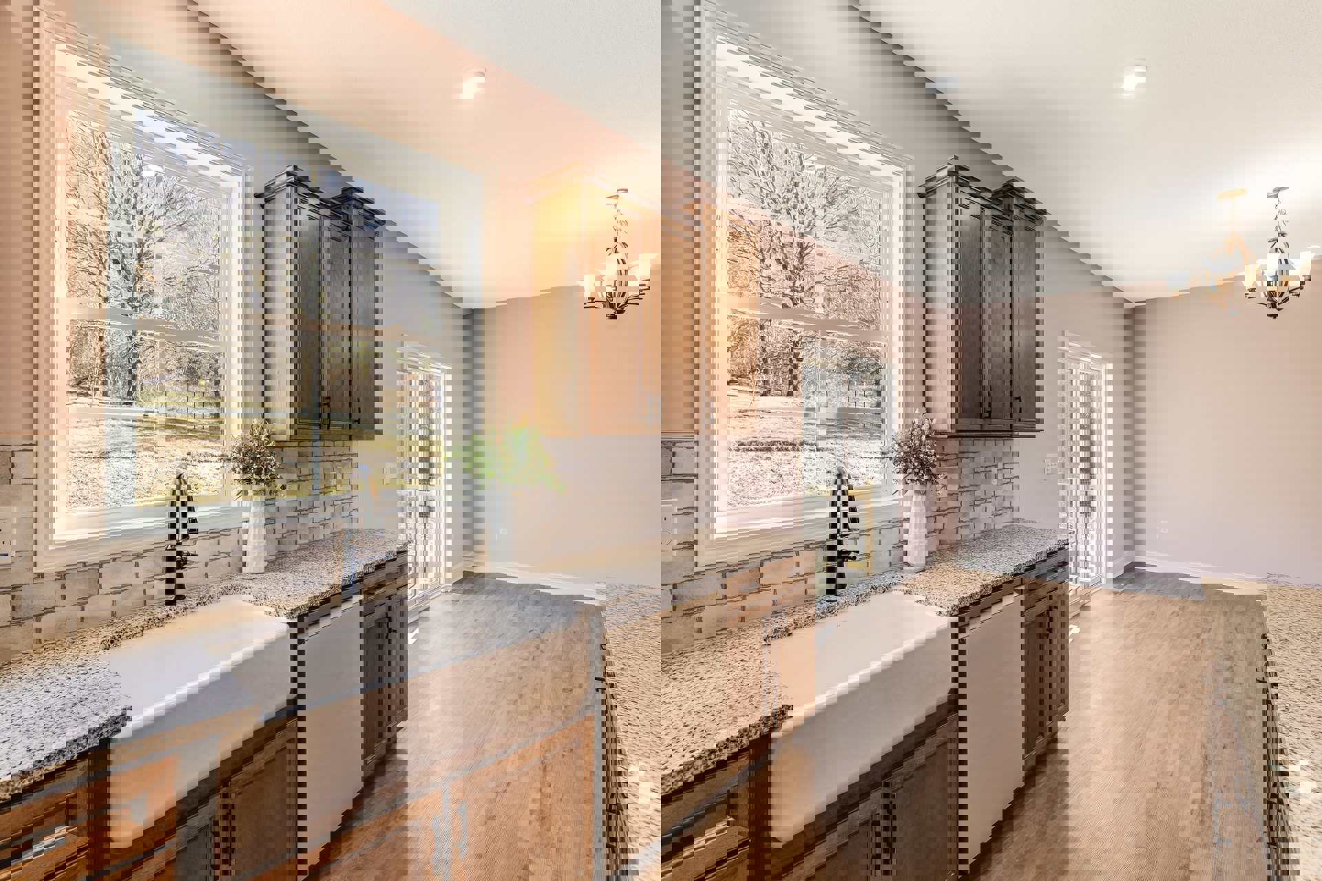 Granite countertop with white undermount sink, white cabinetry, tile floor, vase of flowers, window overlooking tree and grass, brown-framed accent on white wall