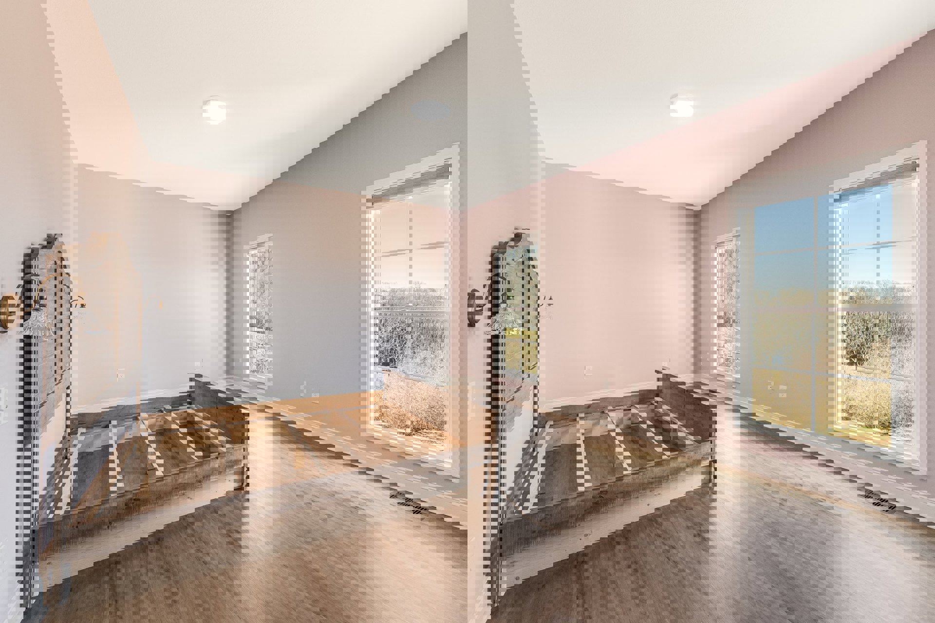 Bedroom with wooden bed frame, hardwood floors, large window overlooking trees, white plaster walls, recessed ceiling light