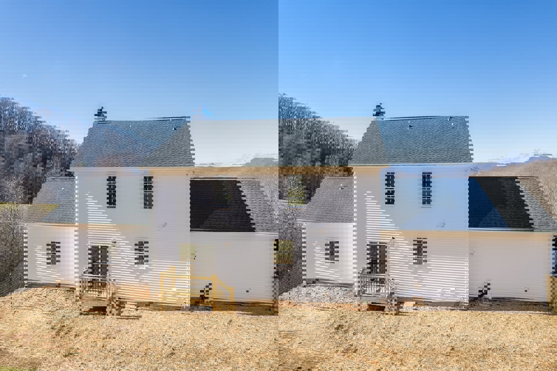 White siding house with blue metal roof, wooden deck with railing, multi-pane white framed windows, surrounded by trees and open sky