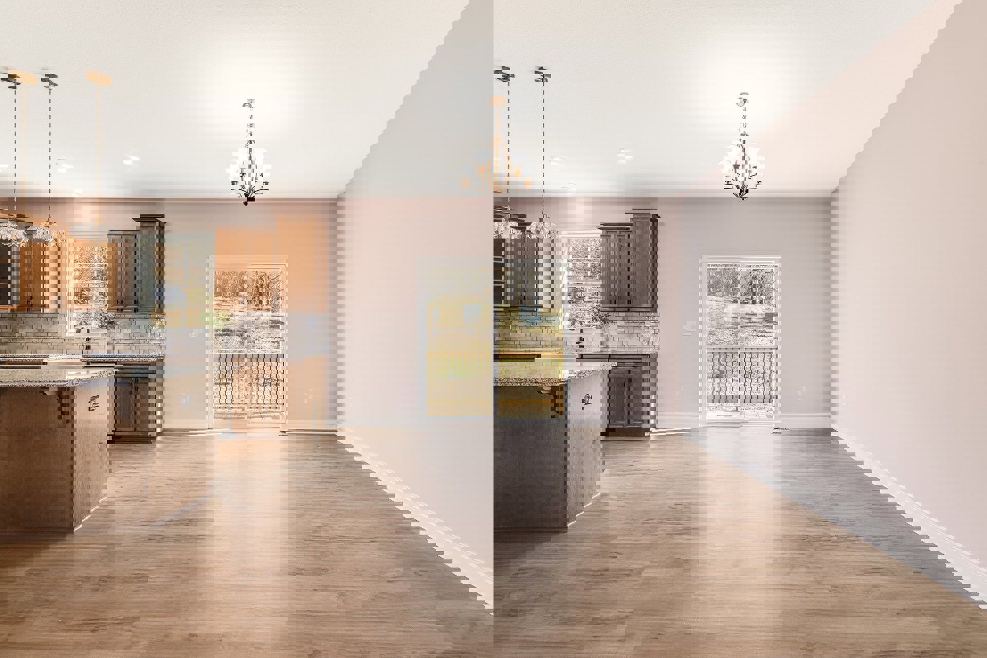 Open kitchen and dining area with wood flooring, white cabinetry, stone countertops, stainless steel appliances, sliding glass door overlooking backyard, modern chandelier above