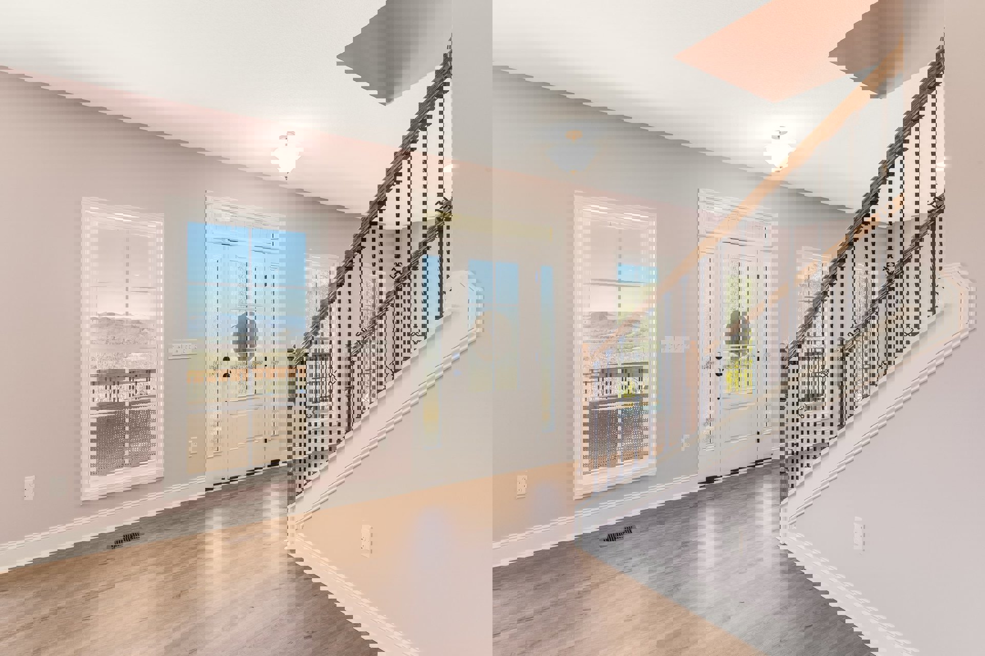 Wood staircase with white balusters and handrail, laminate flooring, plaster walls, large window framing mountain view, round decorative element in window, ceiling light fixture