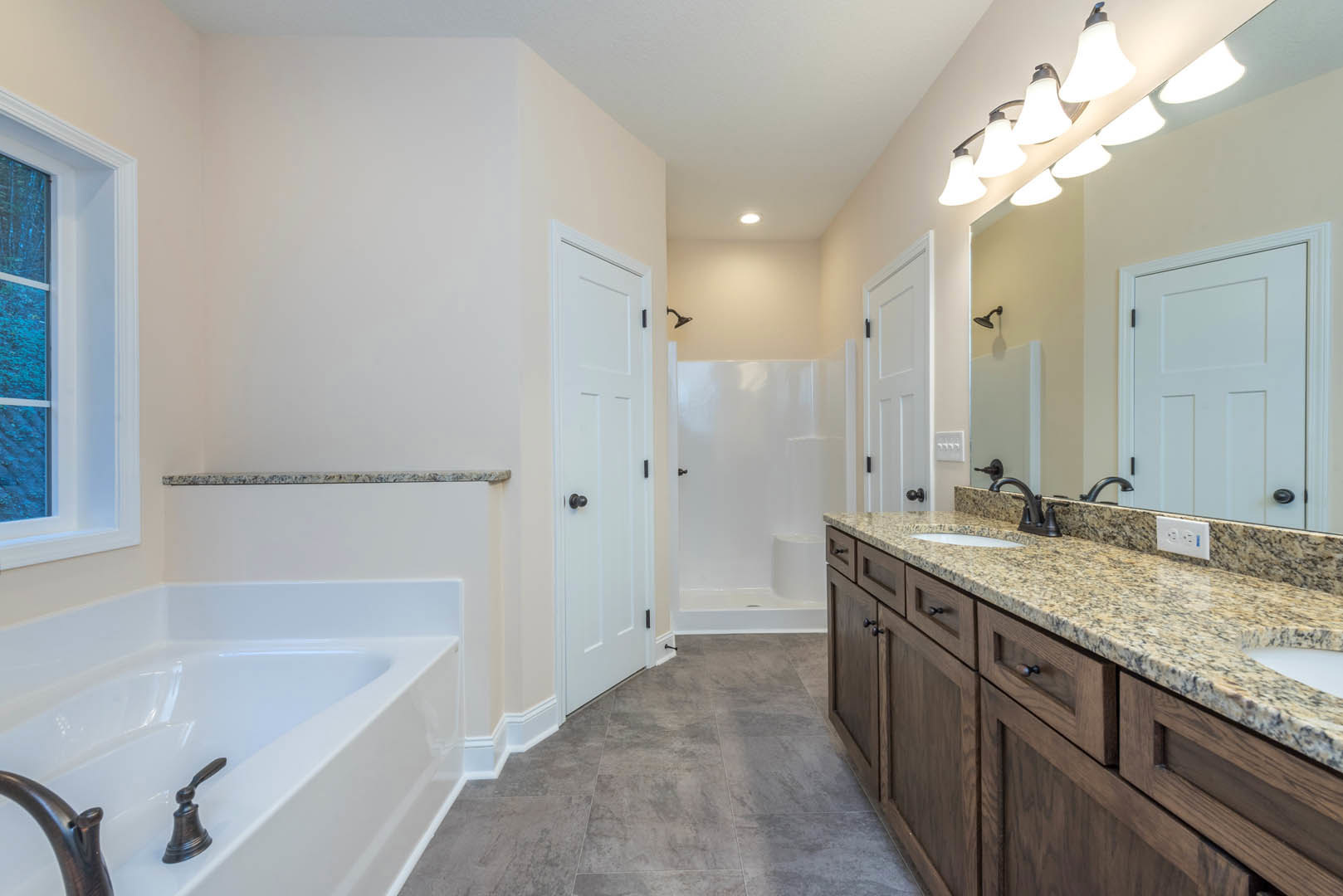 Bathroom featuring a freestanding bathtub with chrome faucet, marble countertop sink, large mirror, white tile walls, and cabinetry.