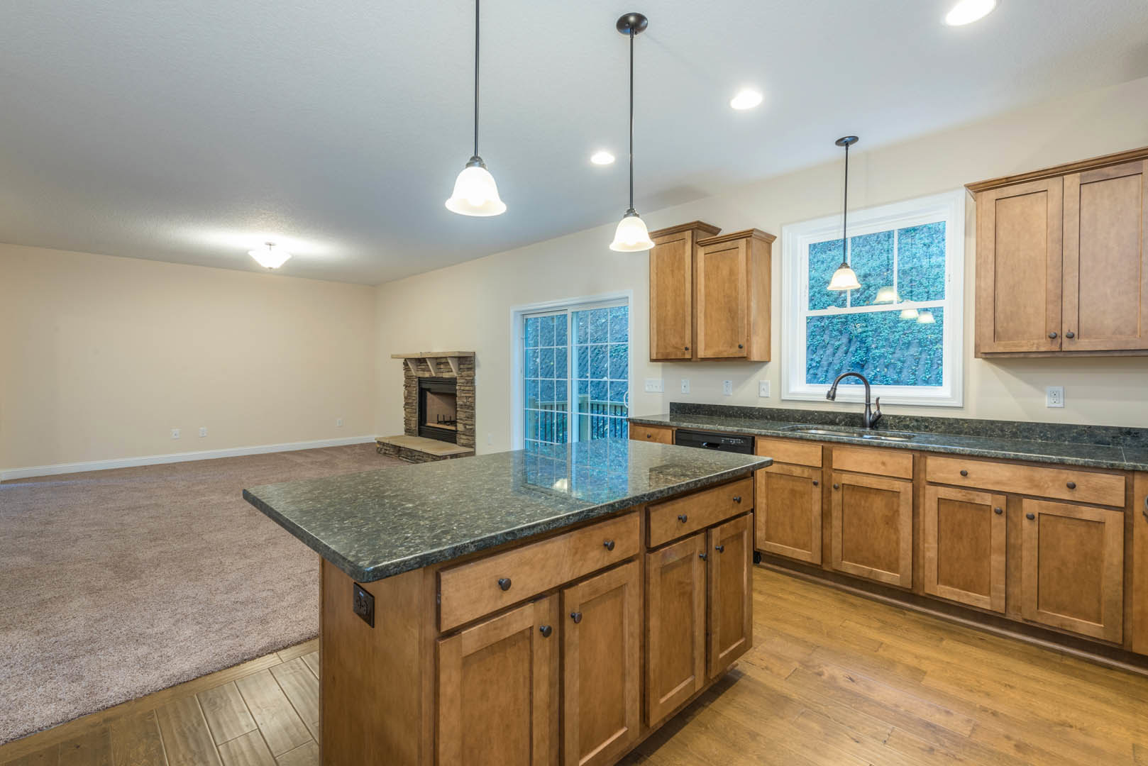 Spacious kitchen featuring a large marble-topped island, white cabinetry, tile backsplash, stainless steel sink, and a window allowing natural light; wood flooring and a fireplace
