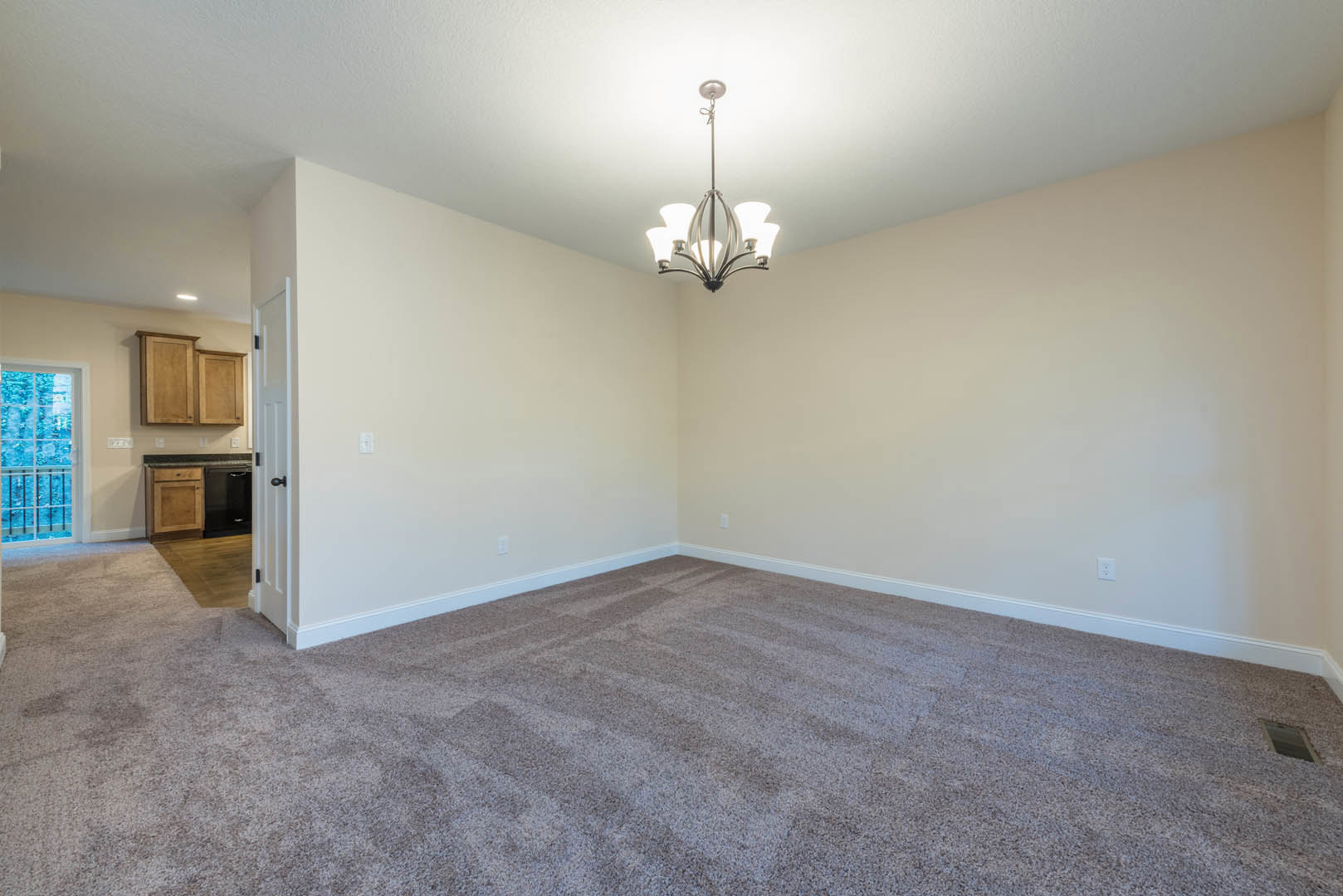 Carpeted living space with white walls, ornate chandelier, large window overlooking snowy forest, and wooden cabinetry along one wall