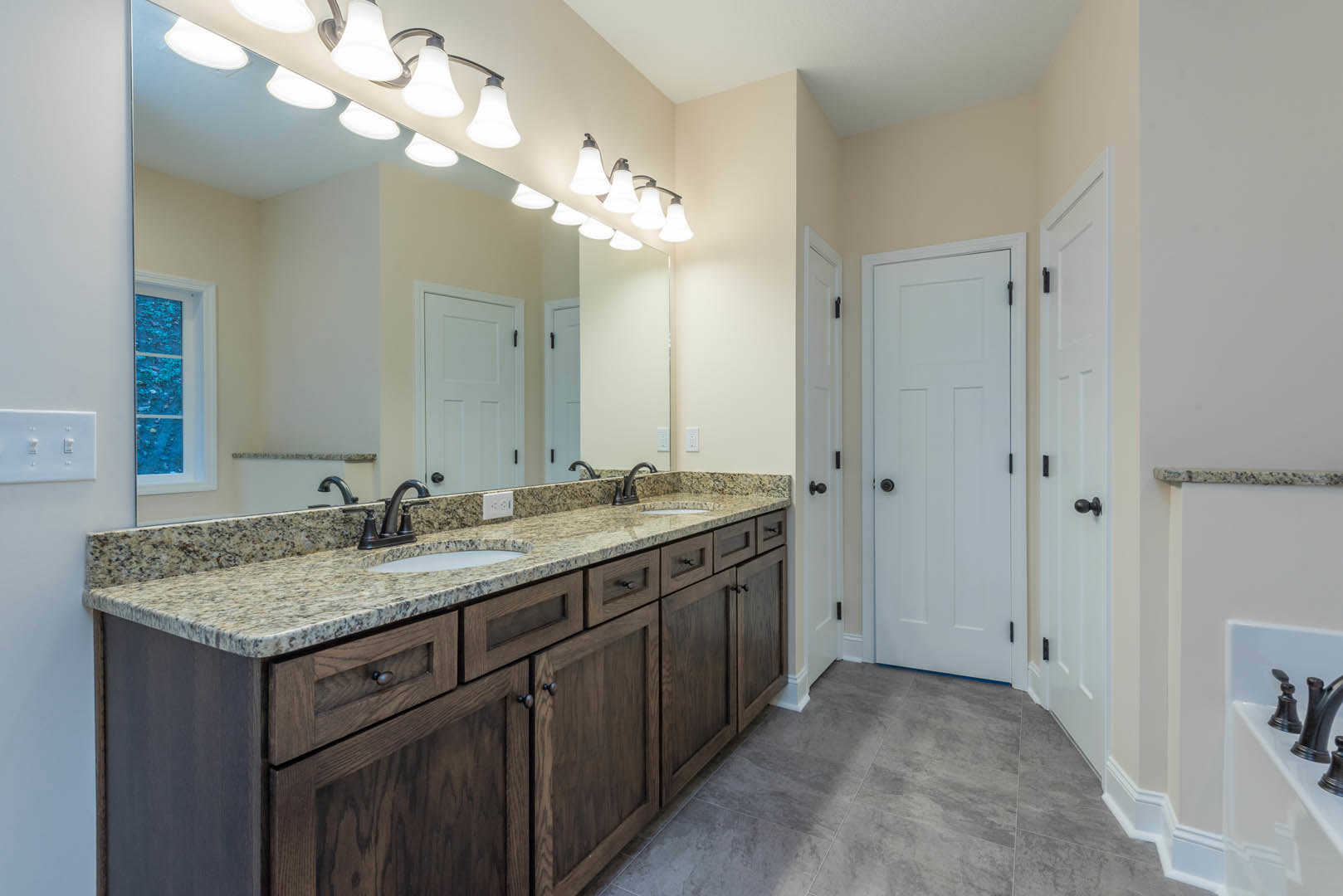 Bathroom with marble countertop, undermount sink, large wall mirror, white cabinetry, black hardware, and white door with black handle