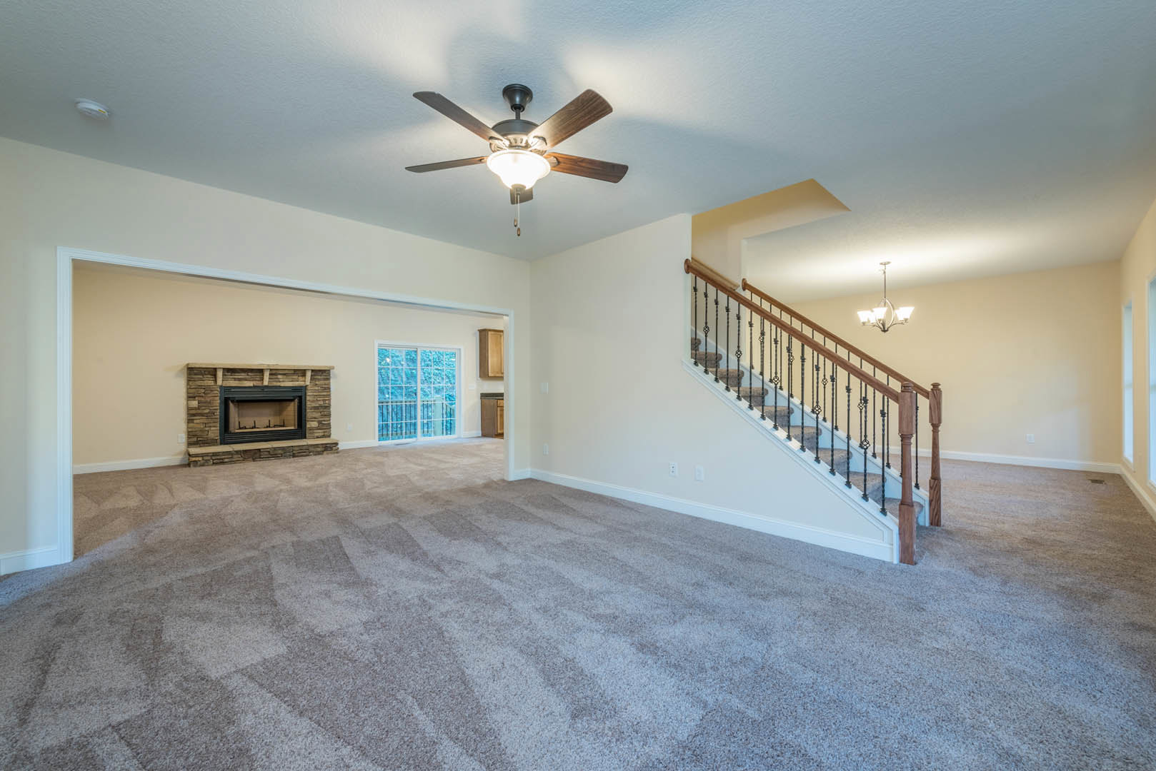 Living room with carpet flooring, central fireplace featuring a black rectangular insert, staircase with wood railing and overhead light fixture, ceiling fan with light, large