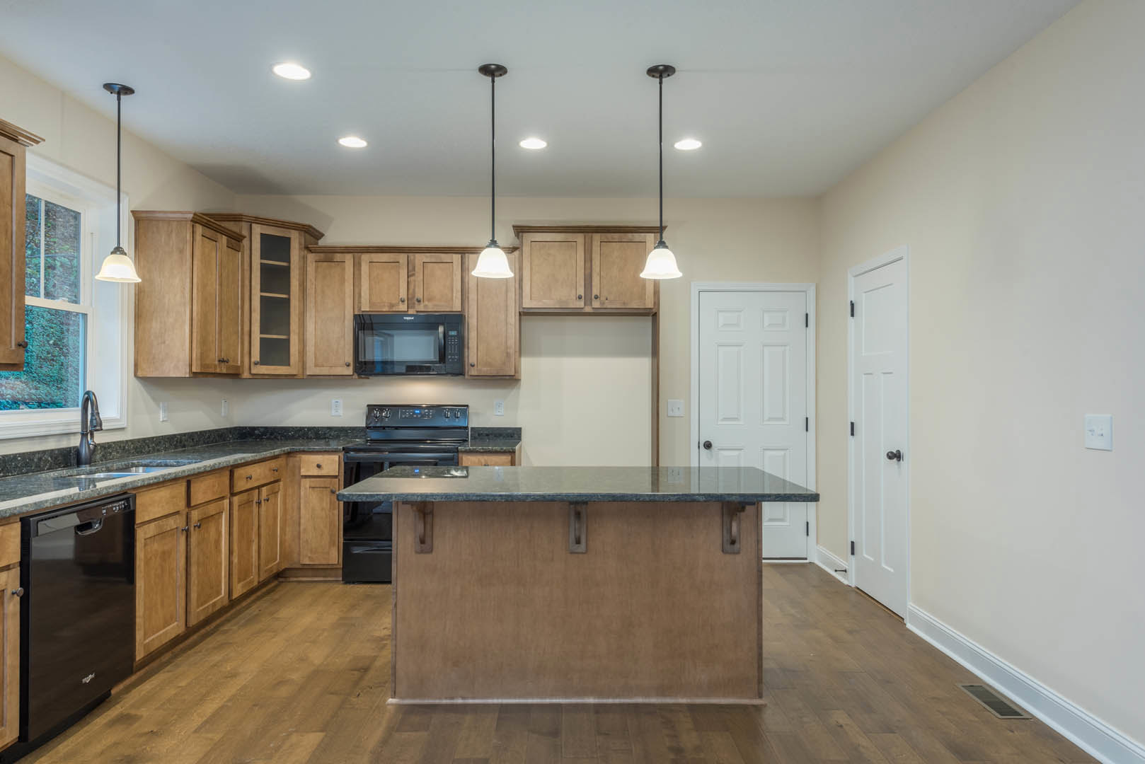 Open kitchen with white cabinetry, stainless steel stove and microwave, large central island with stone countertop, metal bar stools, light wood flooring, and white wall with light